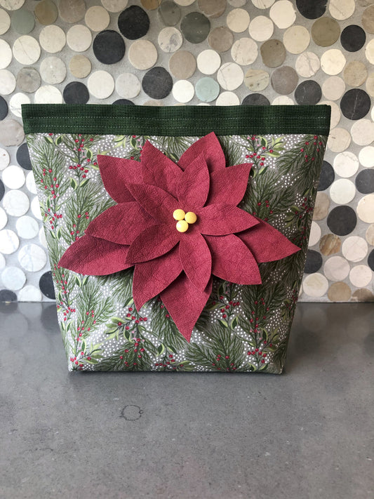 The Free Project Download: Holiday Door Stopper by C&T Publishing is a decorative fabric bag with green and white holiday foliage and a bold red poinsettia with yellow center—perfect for adding festive cheer as a door stopper.