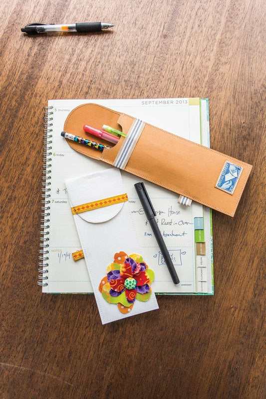 A C&T Publishing Free Project Download: Pencil Case made with kraft-tex holds colorful pens and pencils on a wooden table beside a planner, black pen, and notepad; get free downloadable instructions.