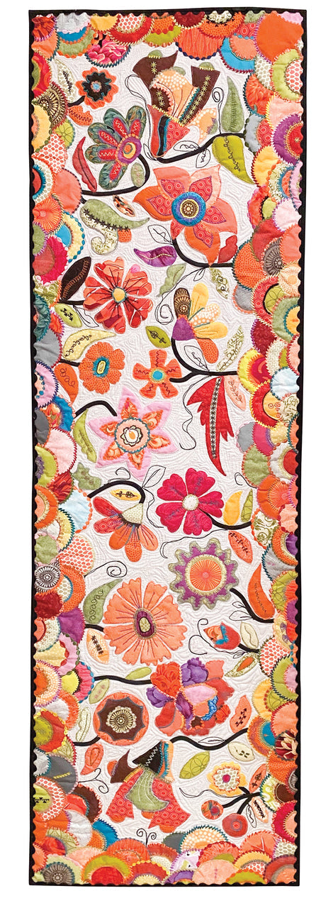 The "Machine Magic" quilt panel by C&T Publishing features colorful embroidered flowers and leaves in orange, red, pink, green, and yellow on white, with scalloped floral borders and decorative stitching.