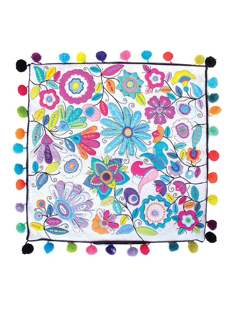 Machine Magic by C&T Publishing is a square textile featuring vibrant floral and leaf motifs with multicolored pom-pom borders. Decorative stitching in bright blues, pinks, purples, yellows, and greens enhances the white background.