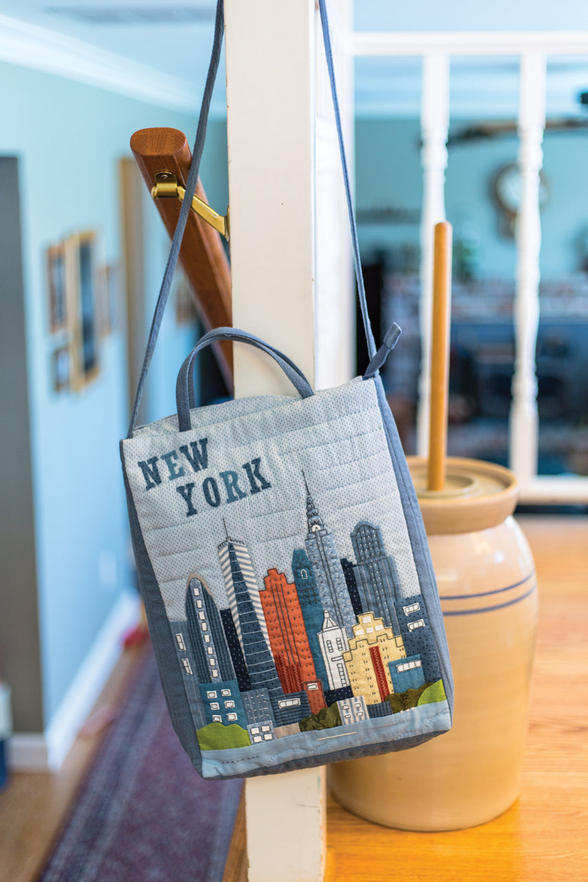 Premium Hand-Appliqué Paper from Masako Wakayama by Stash Books is displayed on a white railing, showcasing heirloom-quality detail, while a large ceramic crock rests on a wooden counter in a cozy, sunlit room.