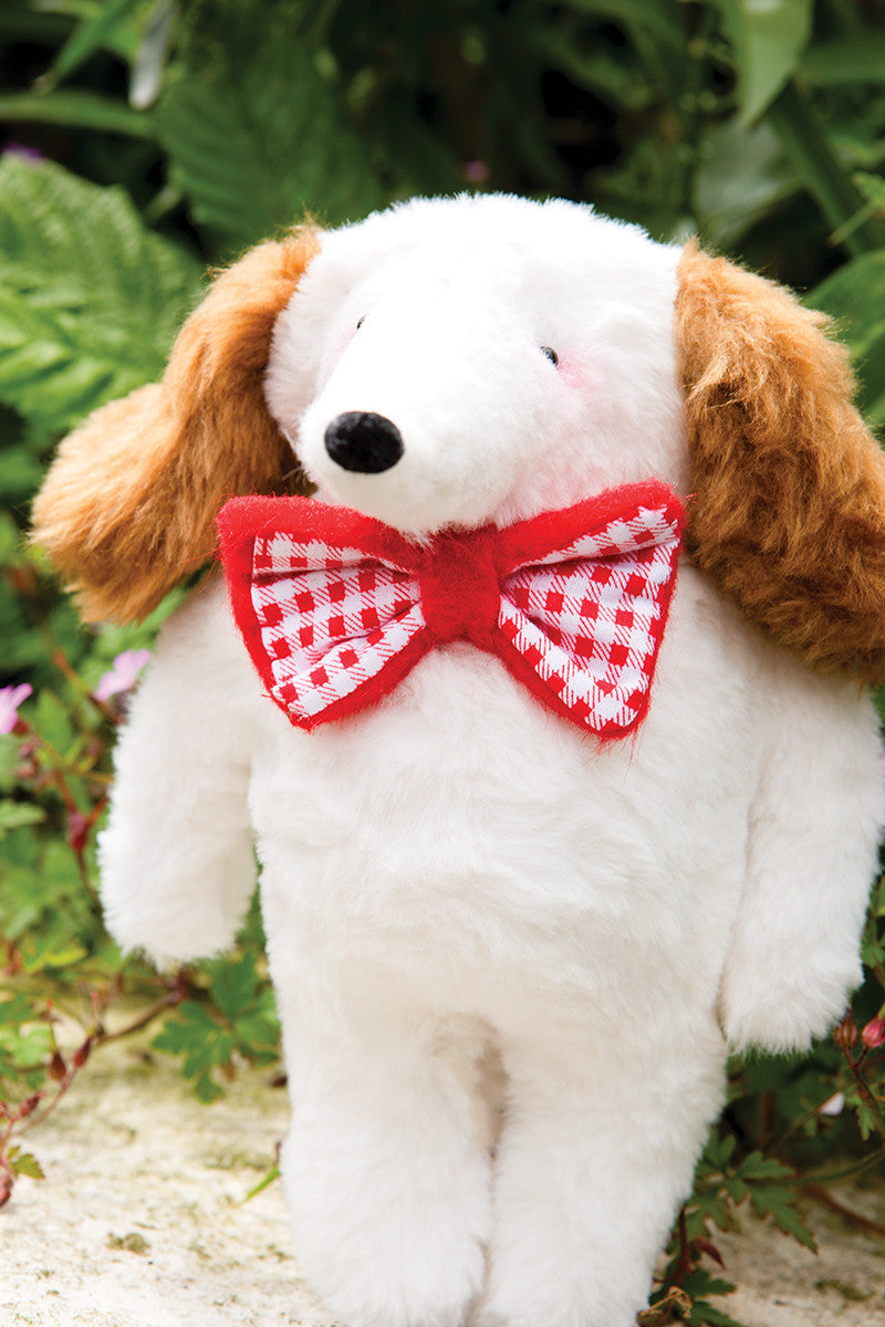 A white plush dog toy with brown floppy ears and a red-and-white checkered bow tie stands outdoors, featured in "Instant Softies" by Stash Books—ideal inspiration for beginner soft toy crafters and handmade stuffed animal enthusiasts.