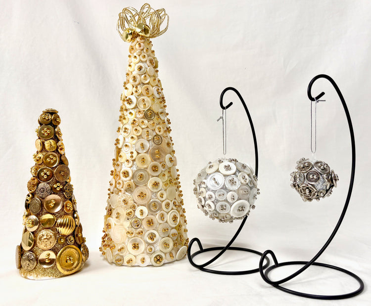 Two cone-shaped trees made of gold and white buttons and two button-covered ornaments hang on black metal stands, all displayed against a white background.