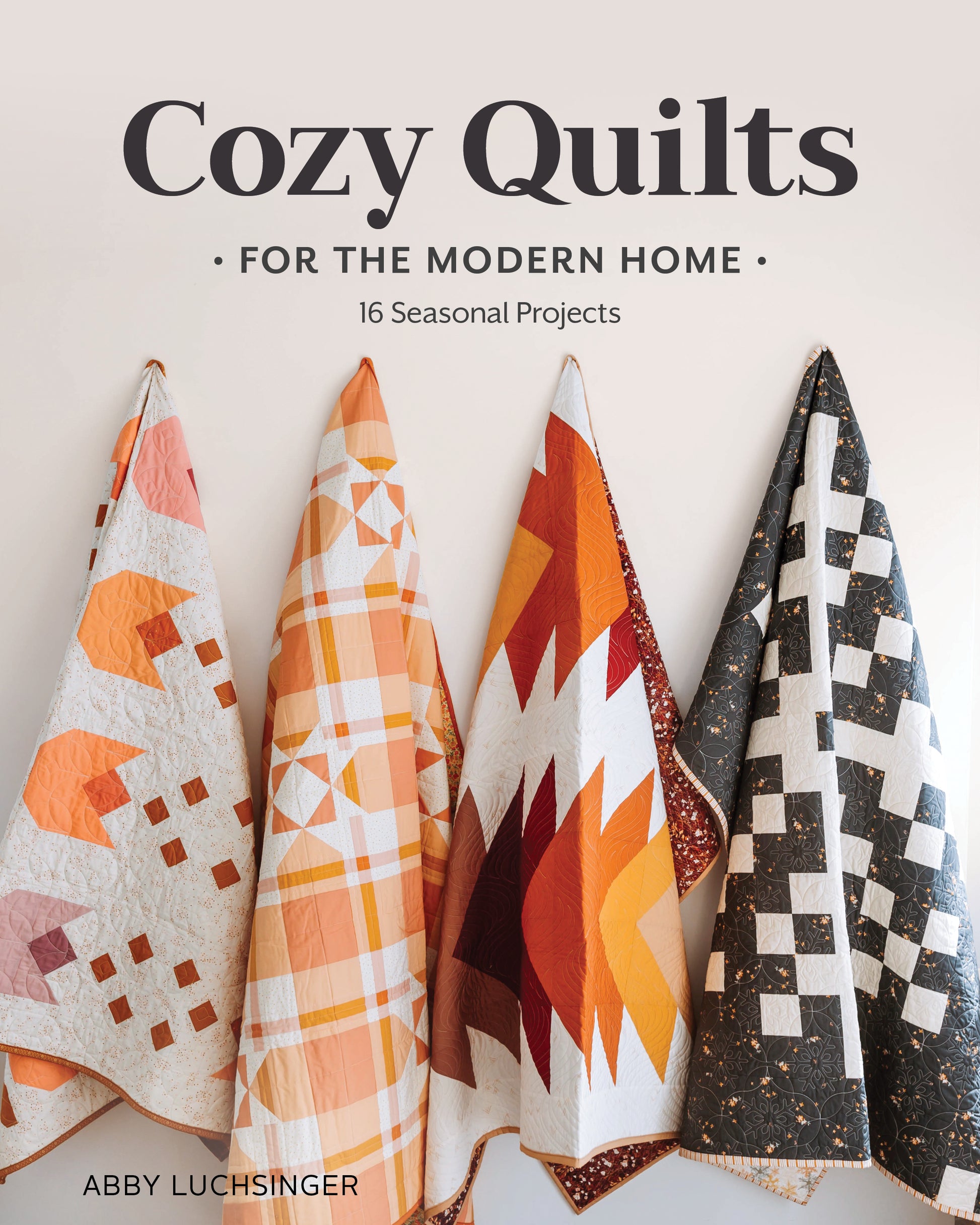 Four vibrant quilts in orange, cream, and black are displayed side by side. The Cozy Quilts for the Modern Home Digital Download from Stash Books offers 16 seasonal quilt patterns perfect for year-round making.