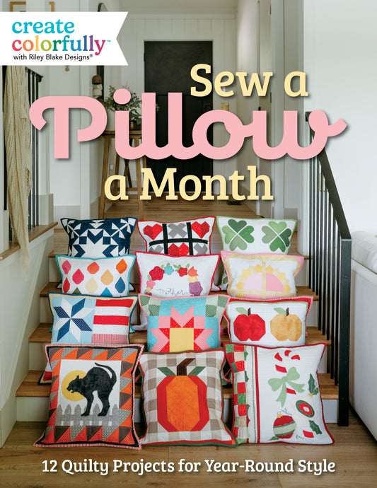 Twelve quilted pillow projects from Sew a Pillow a Month with seasonal themes, including hearts, a cat, a pumpkin, and holiday motifs, displayed on a wooden staircase as part of Riley Blake Designs seasonal decorating.