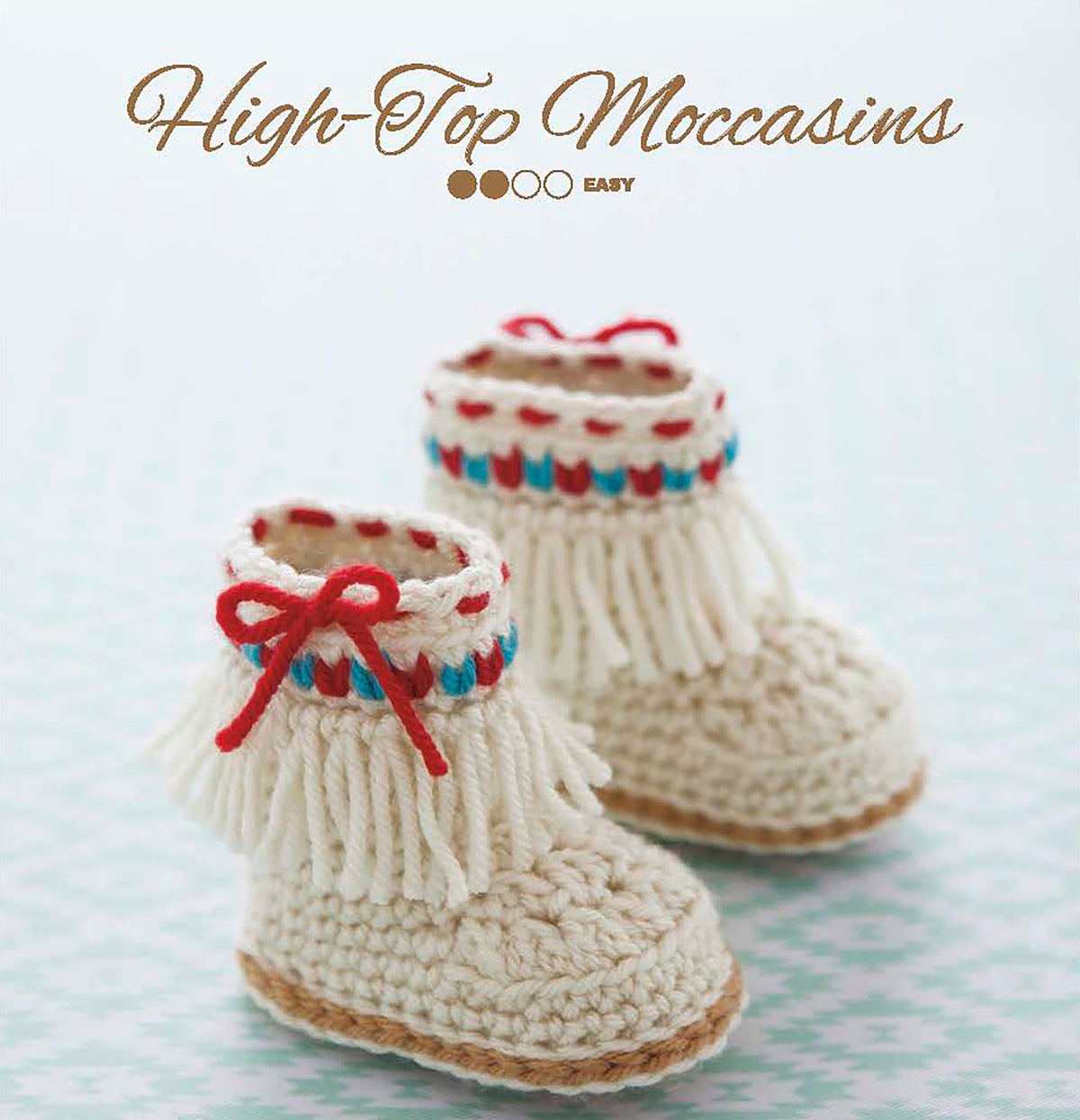 Two crocheted Modern Booties for Baby by Leisure Arts, featuring fringe, red bows, and blue/red accents, rest on a light patterned surface. The text above reads "Modern Booties for Baby" with an easy beginner crochet indicator.
