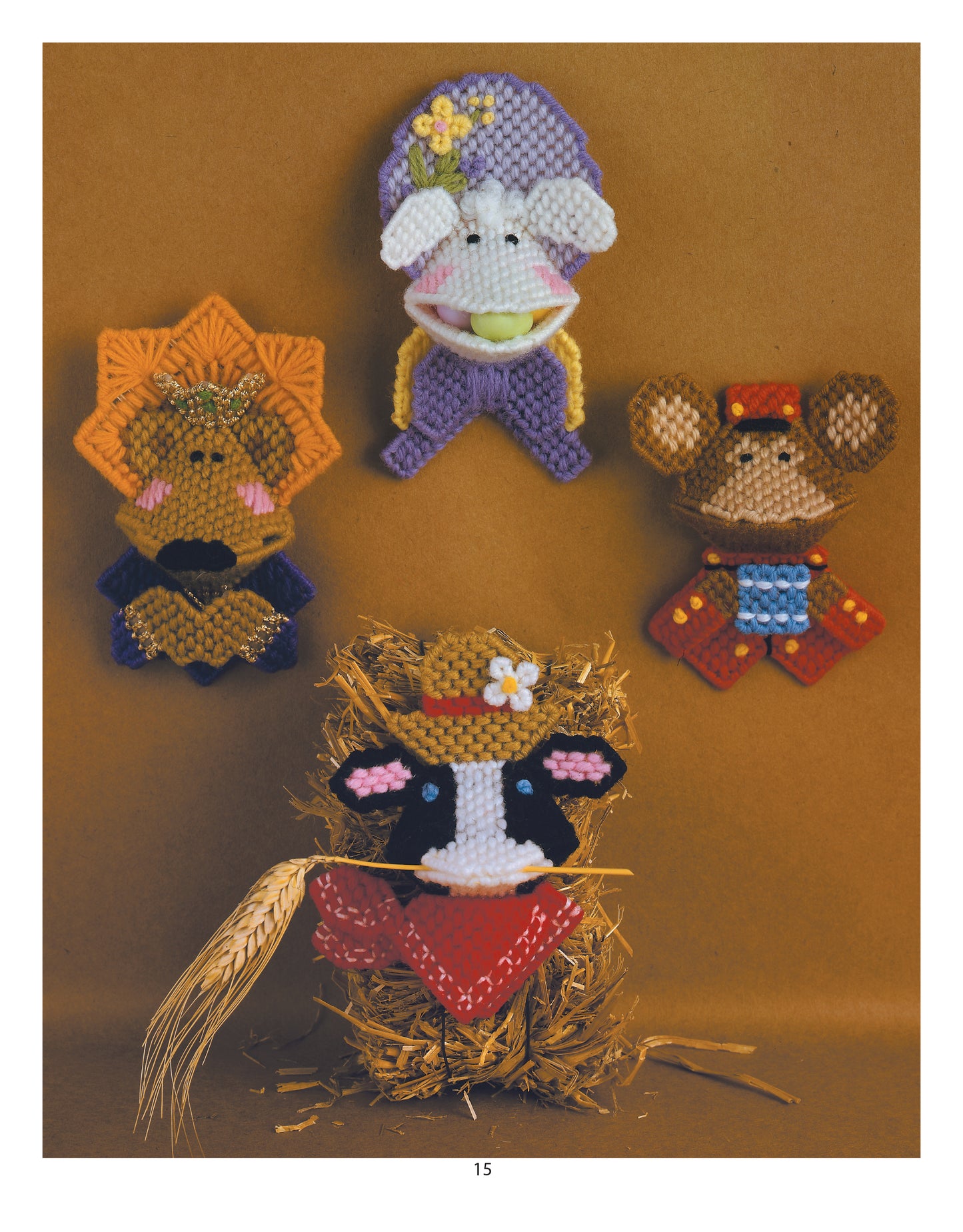 Four playful farm animals made with colorful plastic canvas patterns from the Plastic Canvas Kissers Digital Download by Leisure Arts are displayed: a purple lamb, orange lion, brown mouse, and a cow in a hat with red bandana on hay.