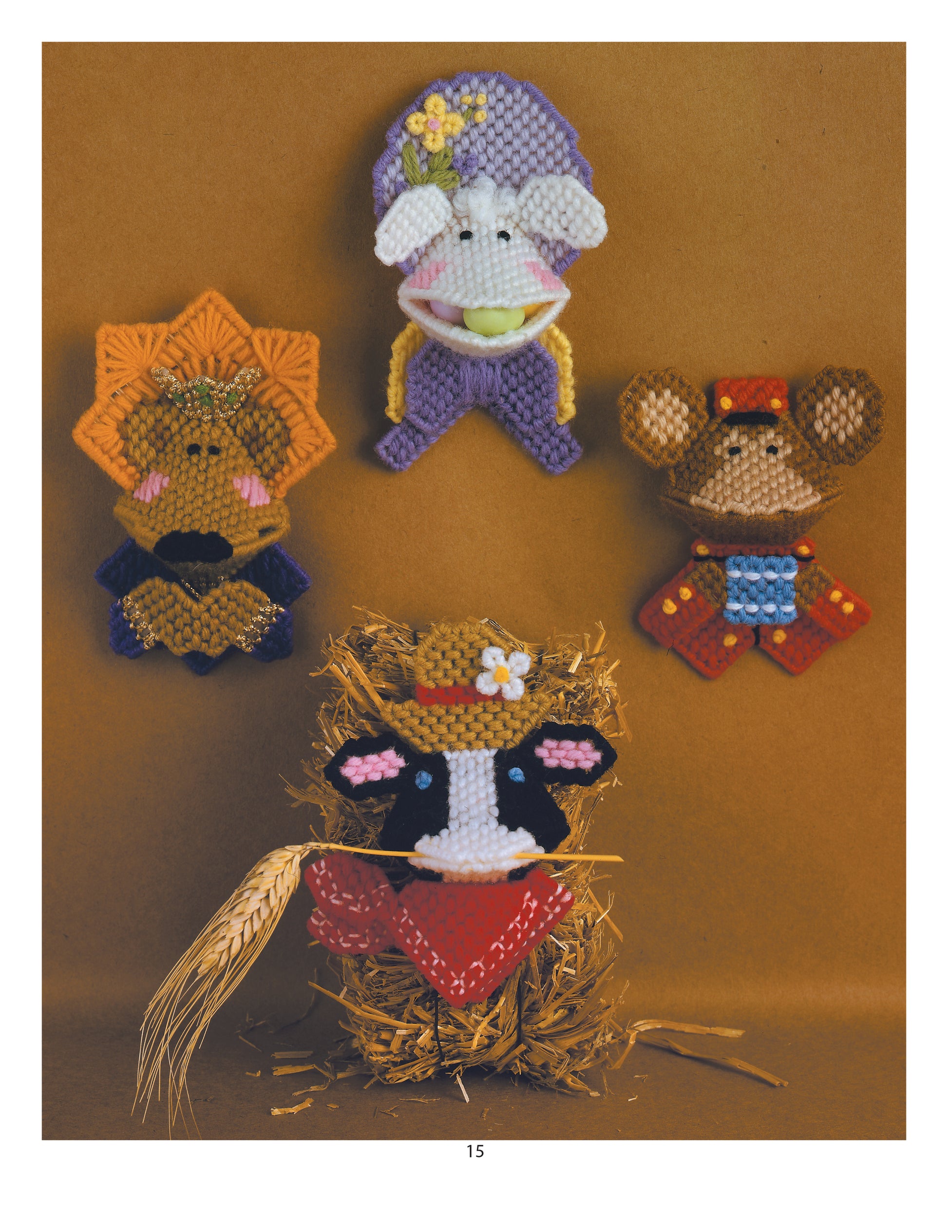 Four playful farm animals made with colorful plastic canvas patterns from the Plastic Canvas Kissers Digital Download by Leisure Arts are displayed: a purple lamb, orange lion, brown mouse, and a cow in a hat with red bandana on hay.