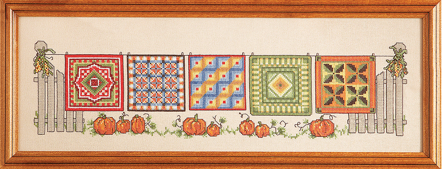 Leisure Arts "Five Seasons of Quilts" features cross-stitched art of vibrant quilts on a white picket fence with pumpkins and vines, displayed in a wooden frame—ideal for quilt pattern enthusiasts.