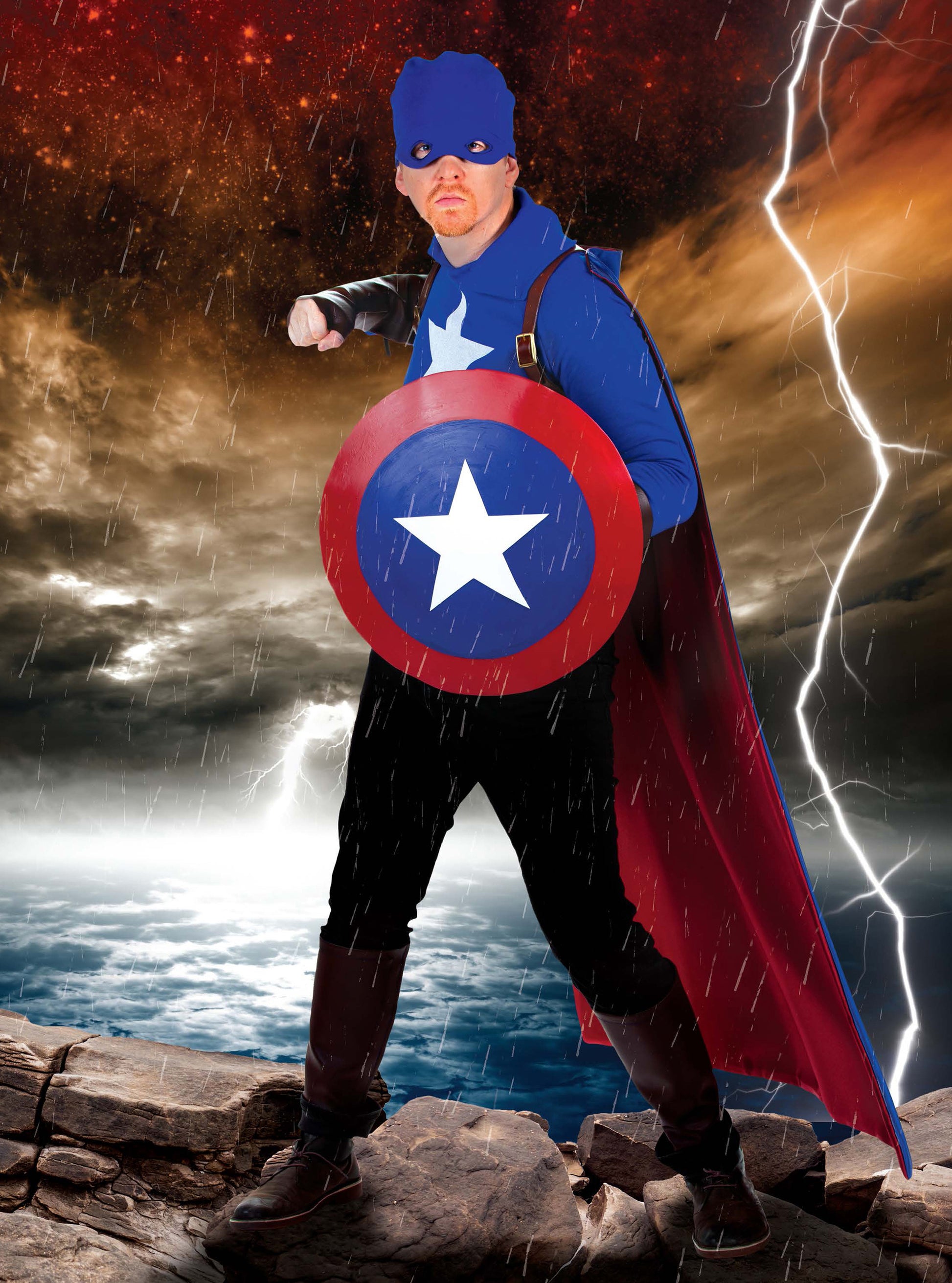 A fan poses in a low-sew superhero costume—with blue mask, star, red and white shield, boots, and cape—on rocky ground in stormy weather. Find DIY costume inspiration in the Cosplay DIY Workbook by Leisure Arts.