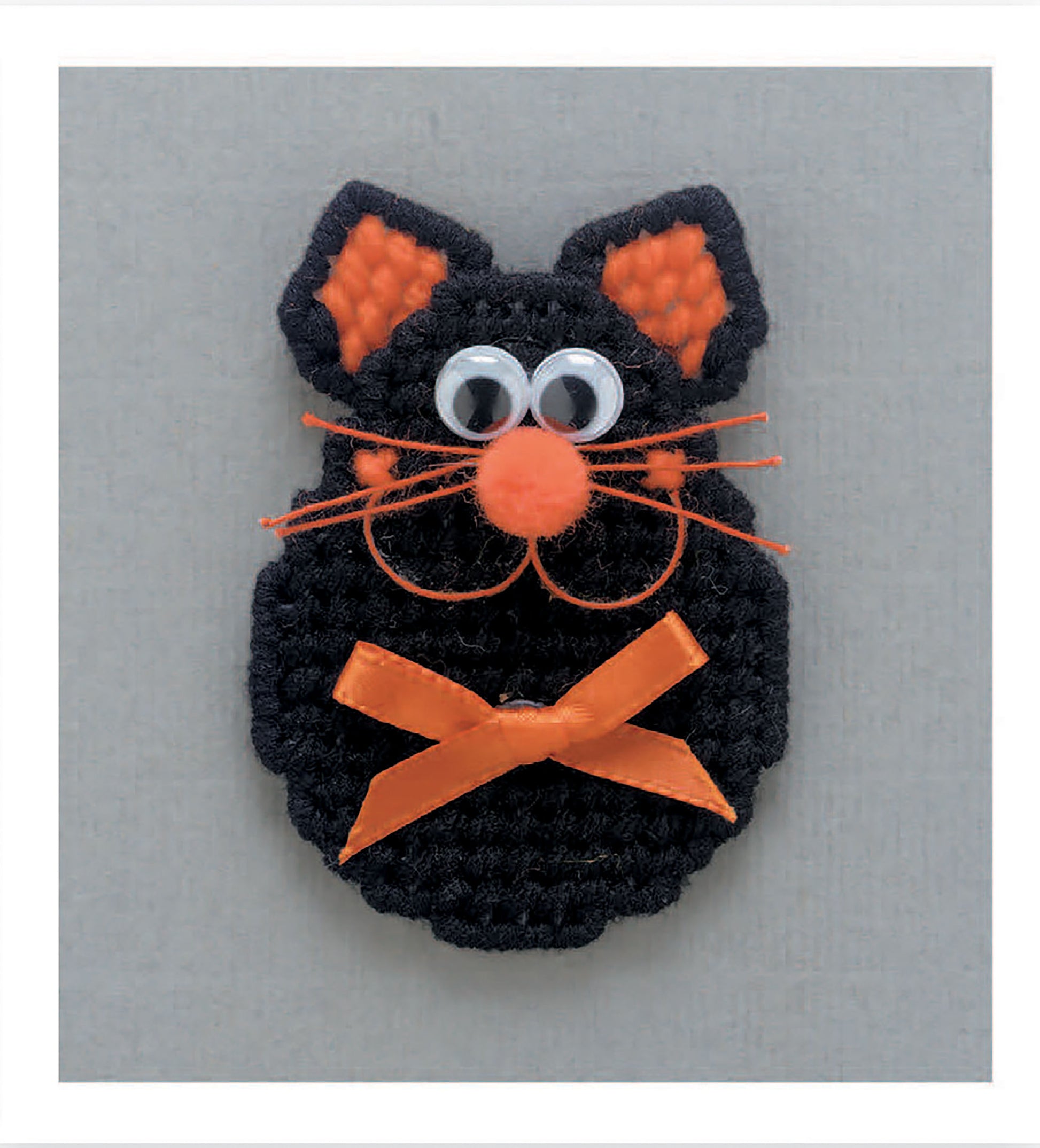 A cute black cat with orange details from Magnet Board Creations in Plastic Canvas by Leisure Arts sits on a gray background—ideal for plastic canvas craft fans. Digital download available.