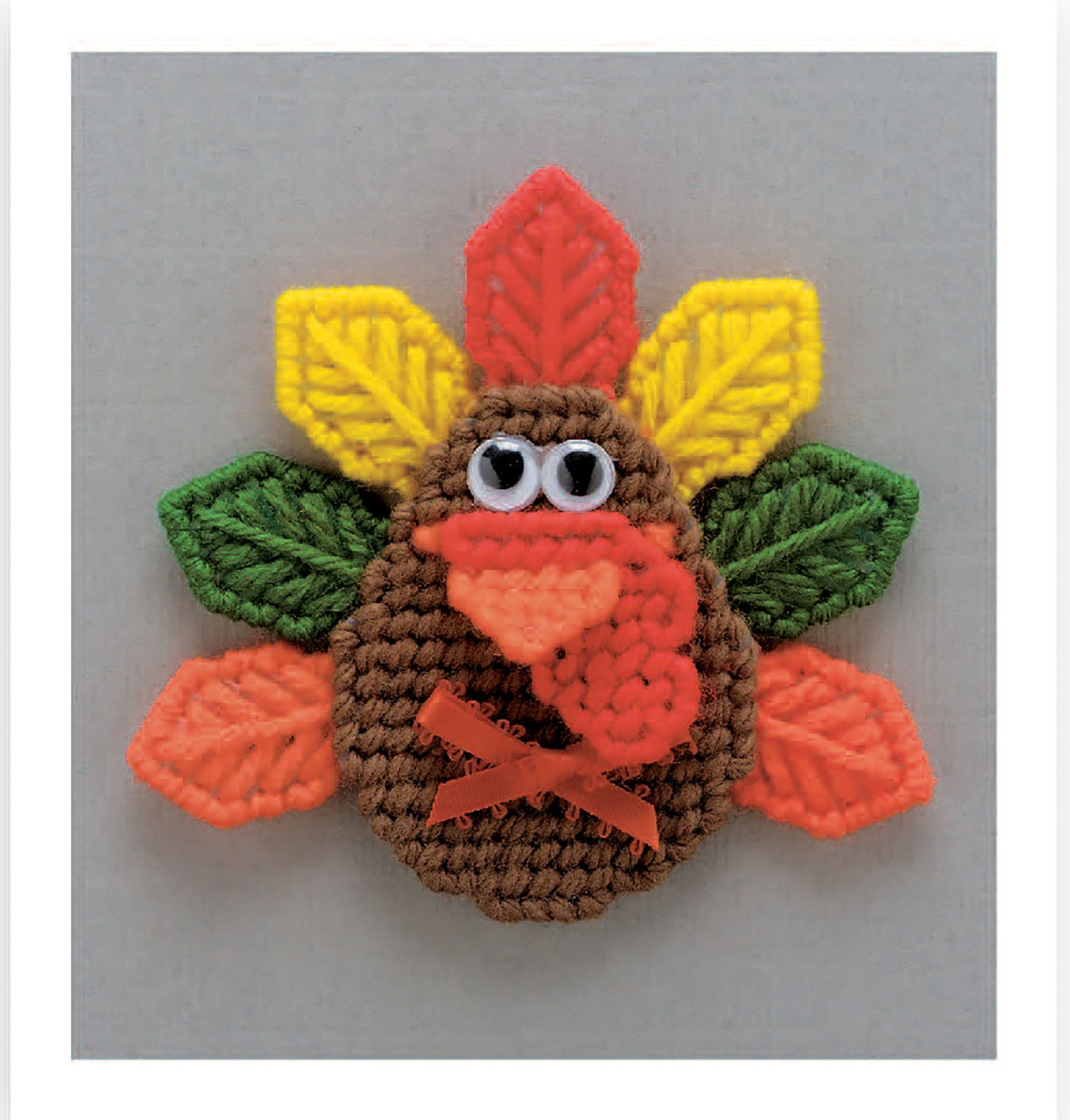 Create adorable turkey designs with googly eyes, orange beaks, and colorful feathers in red, yellow, and green on gray backgrounds using "Magnet Board Creations in Plastic Canvas Digital Download" by Leisure Arts. Perfect for craft lovers!.