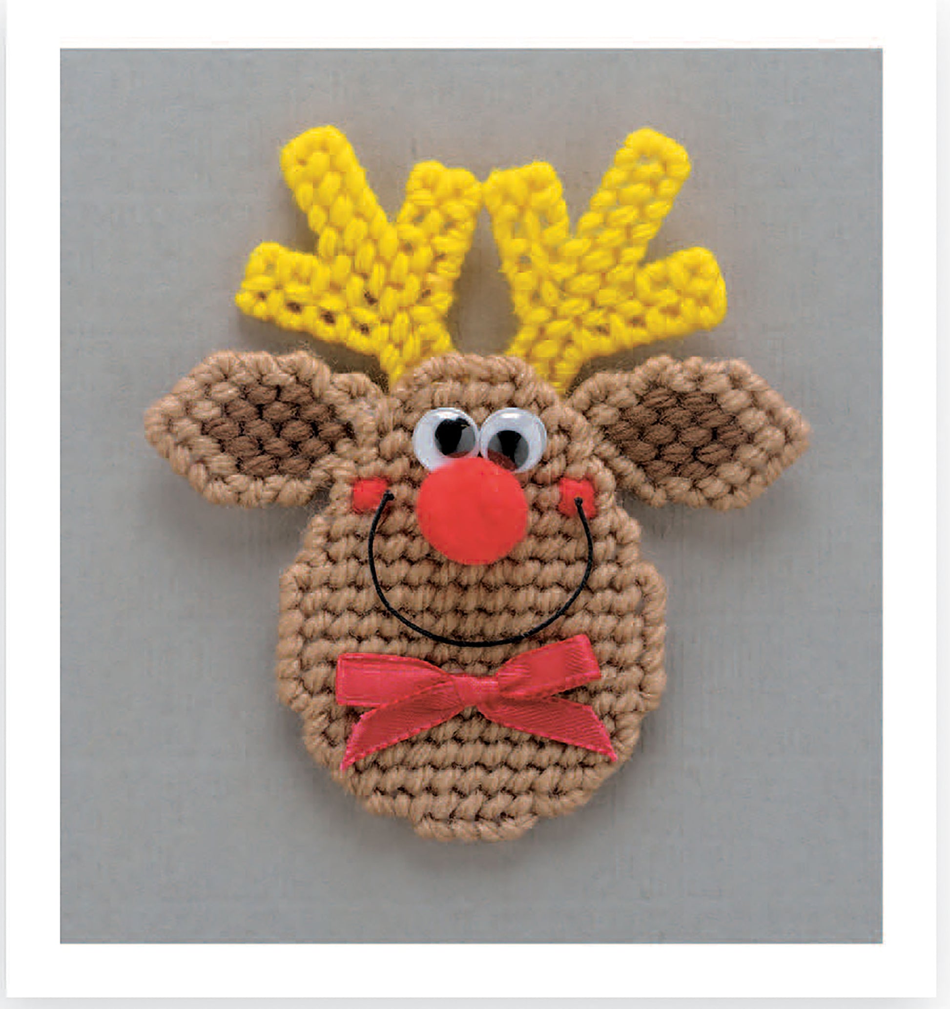 Create a beginner-friendly reindeer face magnet board using the "Magnet Board Creations in Plastic Canvas Digital Download" by Leisure Arts, featuring yellow antlers, googly eyes, a red nose, a smile, and a red neck bow on a neutral background.