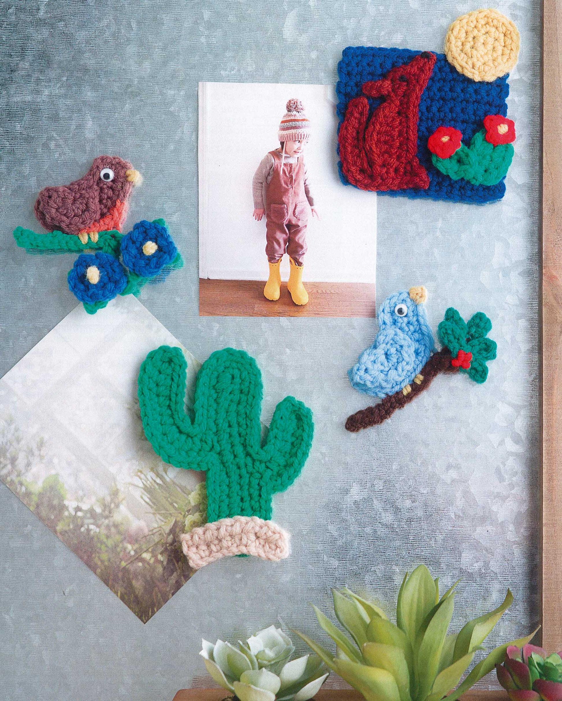 Magnet Board Creations by Leisure Arts displays two photos with crochet magnets shaped like a cactus, bird, blue branch, and landscape—fun accents for your fridge. A small succulent sits below for extra charm.