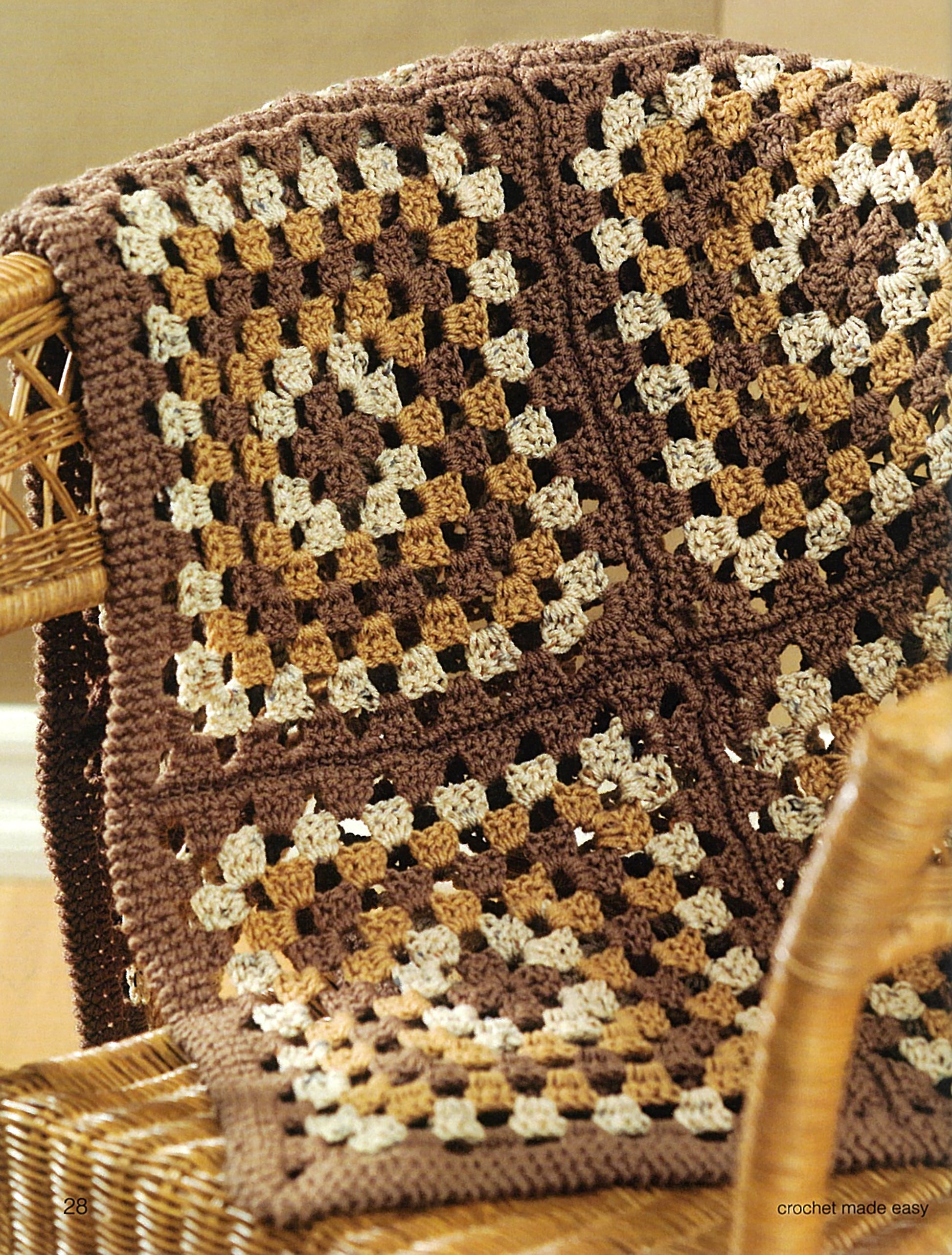 The Leisure Arts "Crochet Made Easy" blanket features a granny square pattern in brown, tan, and cream—ideal for beginners—and is shown draped over a wicker chair.