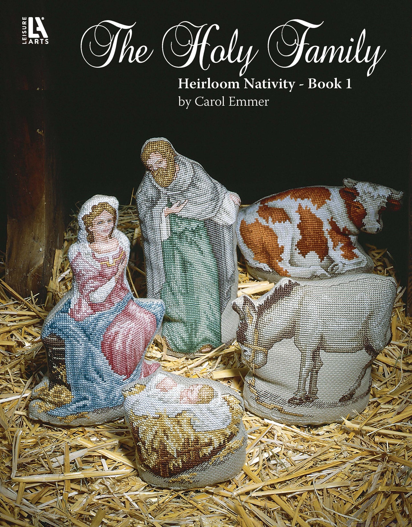 The Holy Family Heirloom Nativity Book 1 by Leisure Arts features a cross-stitch nativity scene of Mary, Joseph, and baby Jesus on straw with a cow and donkey nearby.