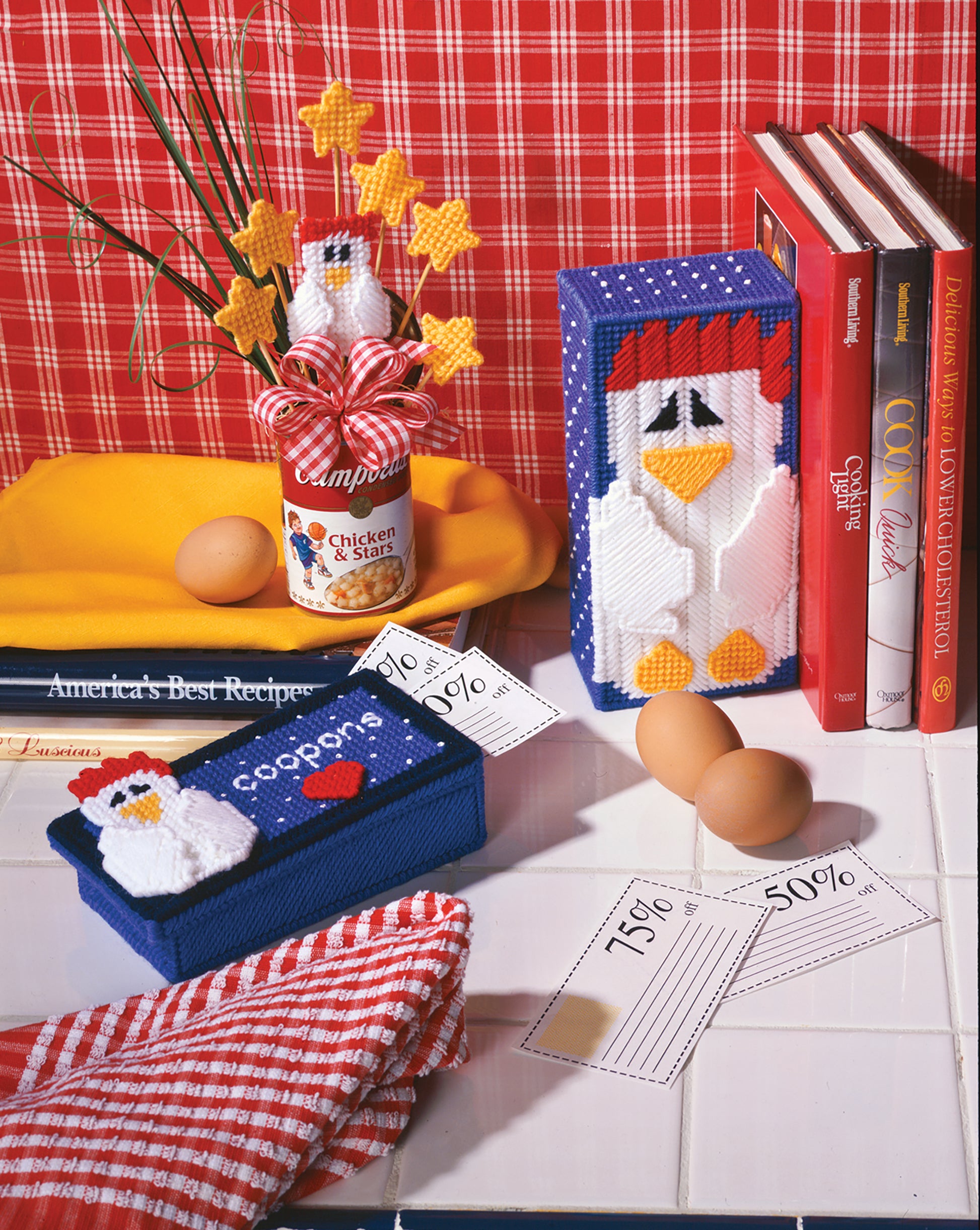 Barnyard Buddies in Plastic Canvas by Leisure Arts features beginner-friendly chicken crafts, a Campbell’s soup can vase with yellow star picks, cookbooks, eggs, and sale tags. Red plaid wallpaper and a checkered towel complete this cozy kitchen scene.
