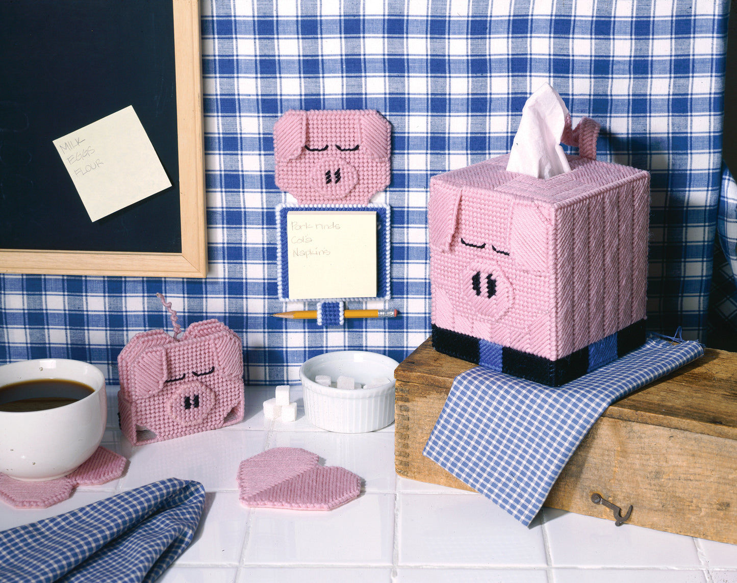 Create a charming kitchen scene with Leisure Arts' Barnyard Buddies in Plastic Canvas—a beginner-friendly set featuring pig-themed pink yarn accessories: tissue box cover, apple-shaped item, note holder, and drink coaster.