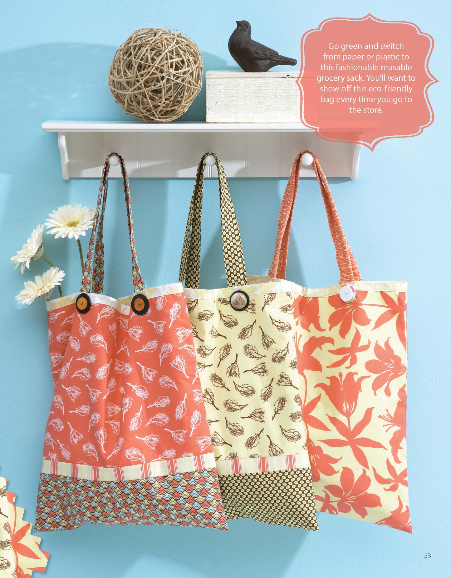 Three vibrant, reusable fabric tote bags made with patterns from Leisure Arts’ "It’s in the Bag! Digital Download" hang below a shelf with daisies, twine, and a bird figurine against a light blue wall—ideal for beginner sewing projects.