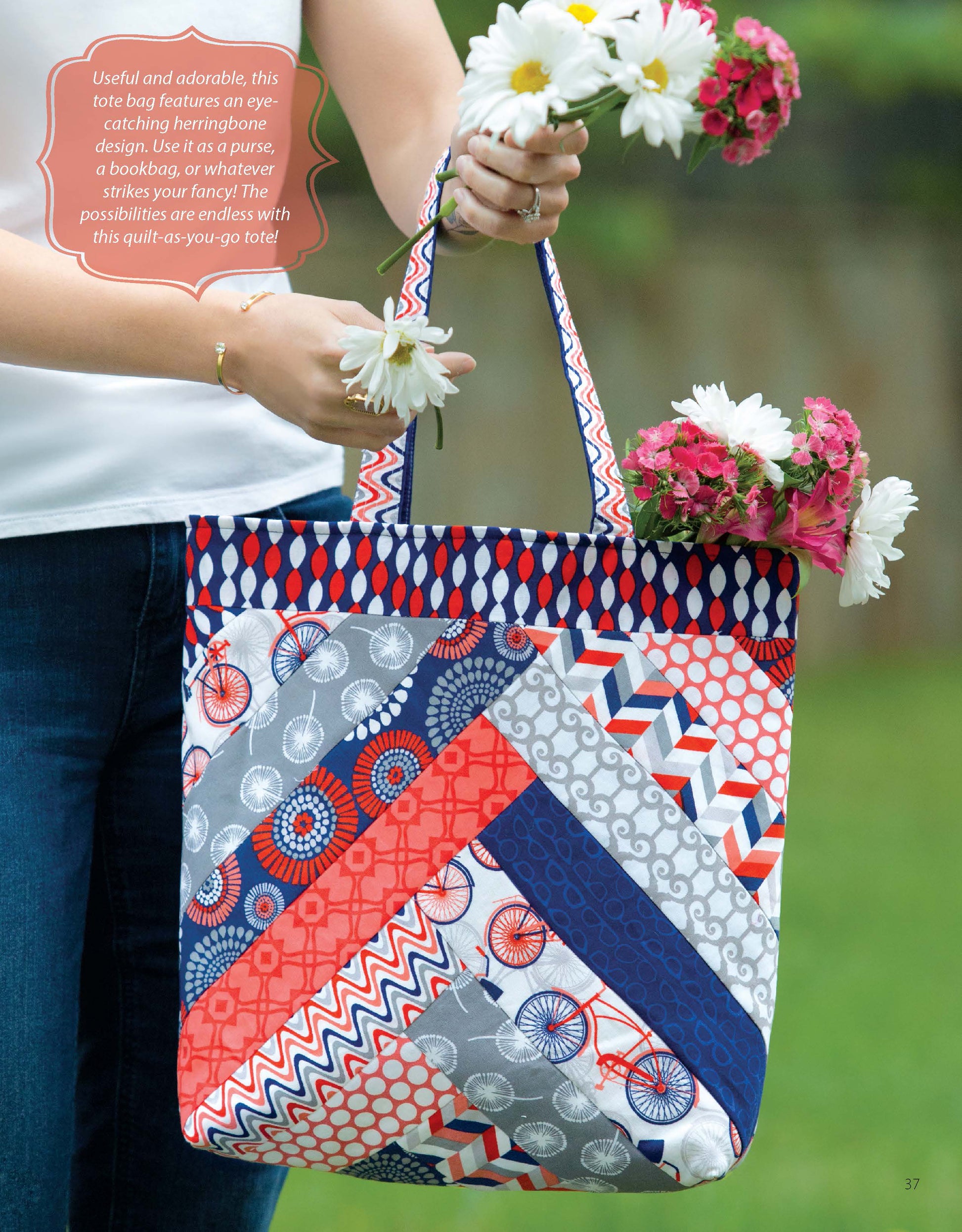 A person holds a tote made with the It's in the Bag! Digital Download by Leisure Arts, featuring geometric and floral prints in red, white, blue, and gray, plus pink and white flowers. The outdoor scene is ideal for beginner sewing projects.