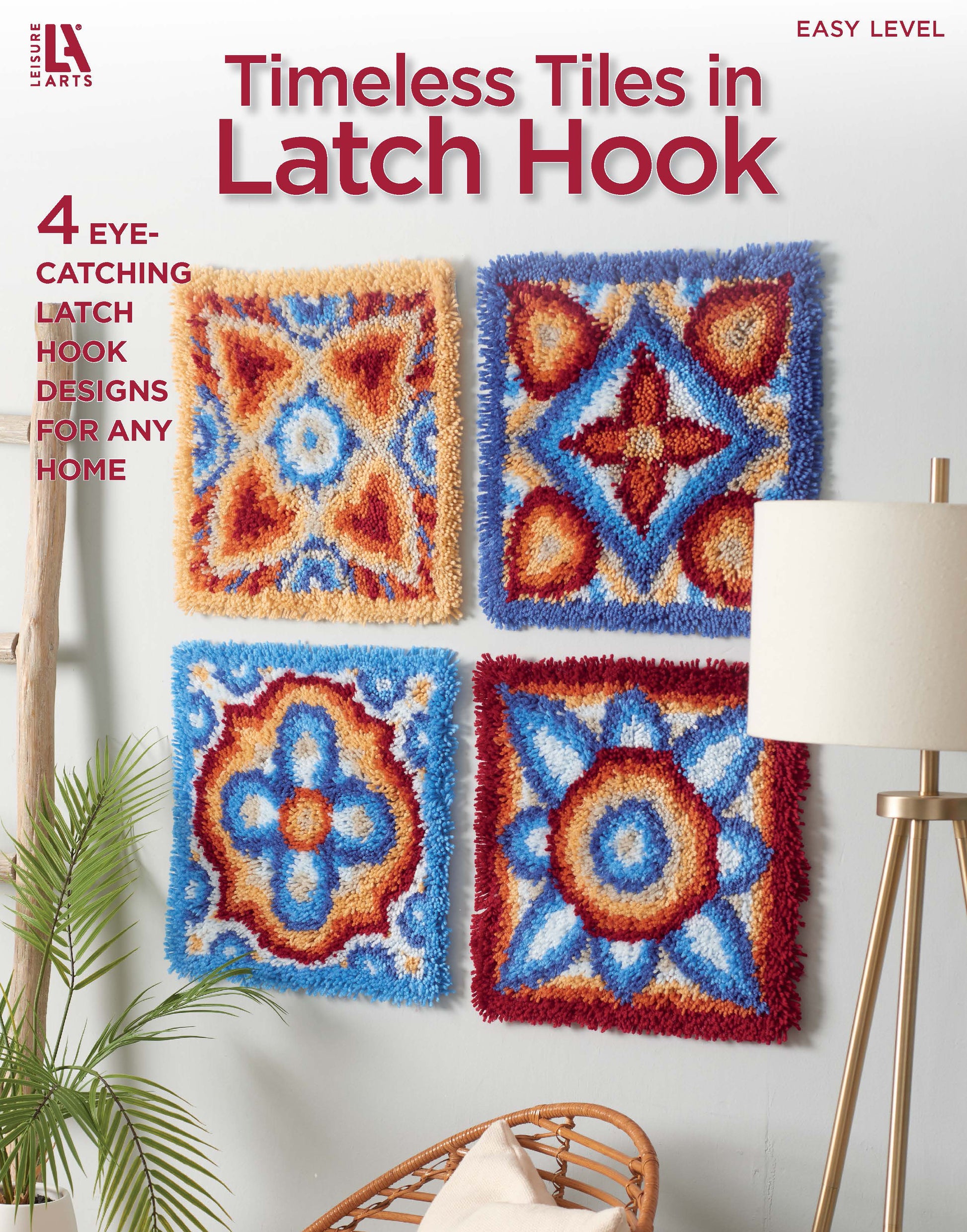 Four vibrant latch hook designs in blue, red, yellow, and orange from Leisure Arts’ Timeless Tiles in Latch Hook hang on a light wall above a plant and lamp. Features beginner-friendly patterns with color charts for home décor.