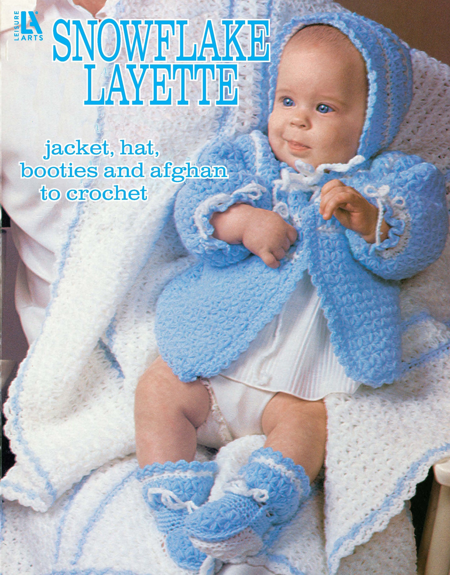 A baby in a blue crocheted jacket, hat, and booties sits on a white afghan. Text: Snowflake Layette to Crochet by Leisure Arts uses snowflake stitch for matching blanket, jacket, hat, and booties.