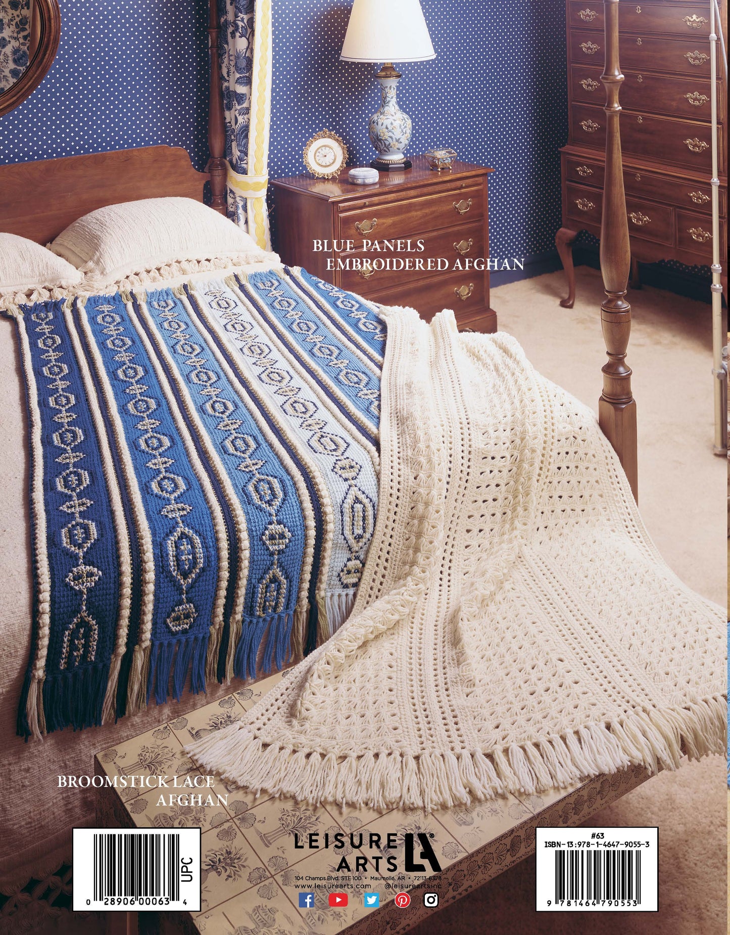 A neatly made bed displays blue embroidered and white broomstick lace afghans with fringe, showcasing hand-sewn charm. Featured: patterns from "The Afghan Book" by Leisure Arts. Vintage décor with wooden furniture and blue wallpaper.