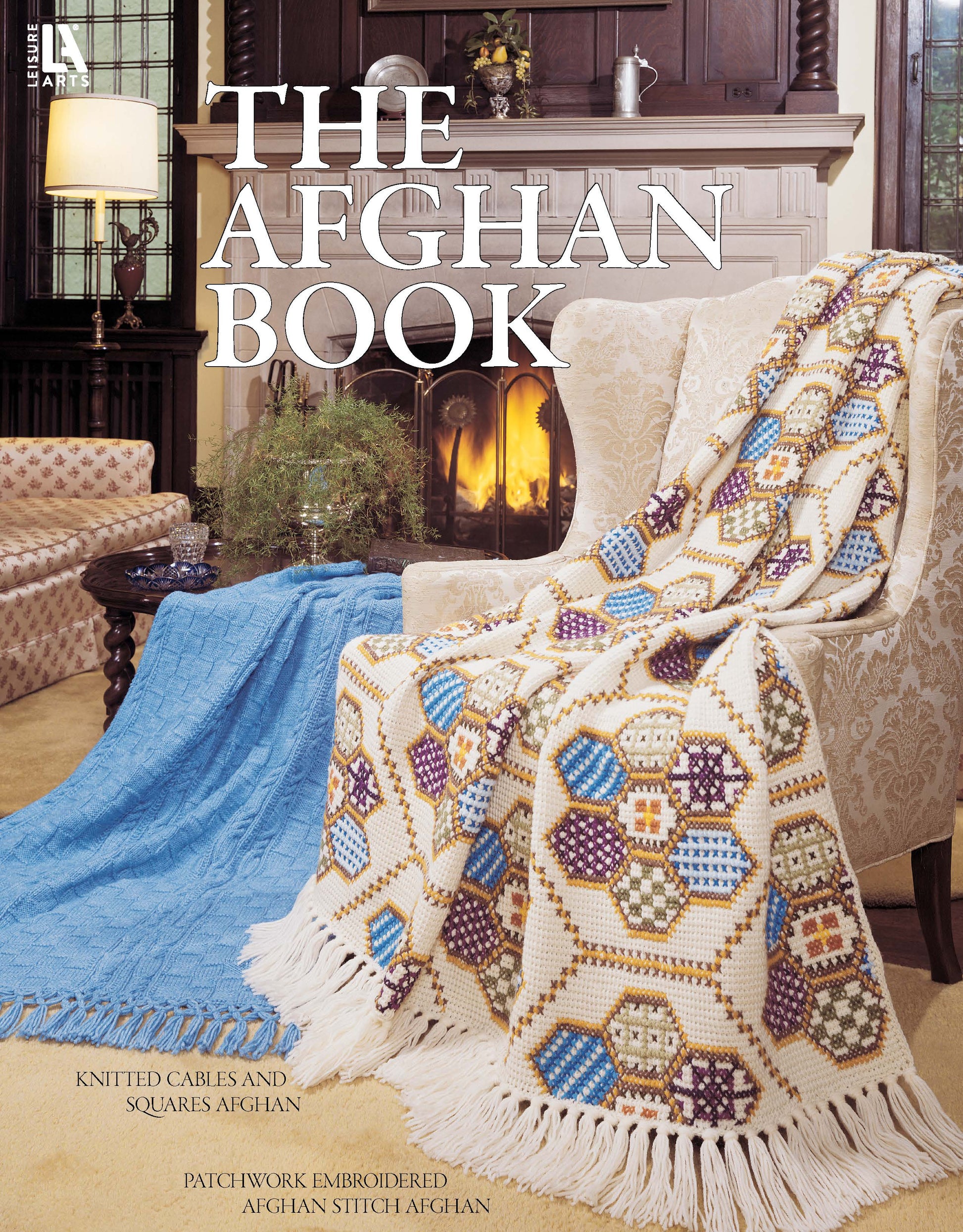 A cozy living room features a cream armchair with a colorful patchwork afghan and a table topped by a blue embroidered afghan. "The Afghan Book" by Leisure Arts is shown, with pattern descriptions displayed below.