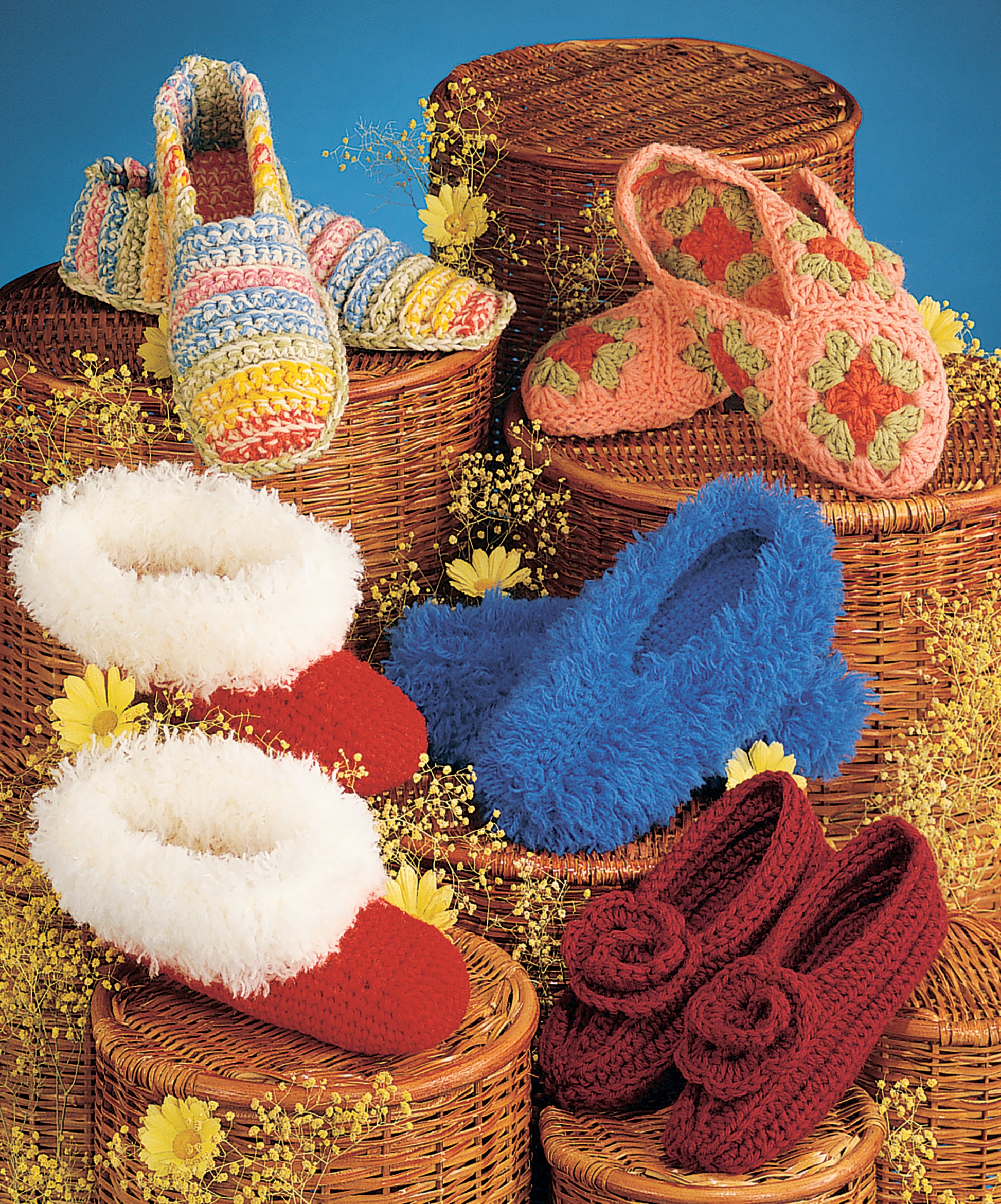 Leisure Arts Crocheted Slippers for Women & Children are displayed in five colorful pairs on woven baskets decorated with yellow flowers, set against a blue background. Styles include crocheted, fluffy, and rose-adorned designs.