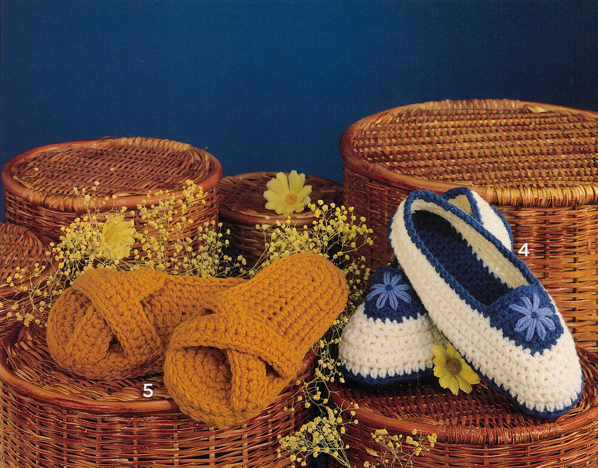 Two pairs of Leisure Arts Crocheted Slippers for Women & Children, in yellow or white with blue trim and floral accents, are displayed on wicker baskets with yellow flowers. Each pair is labeled 4 and 5.