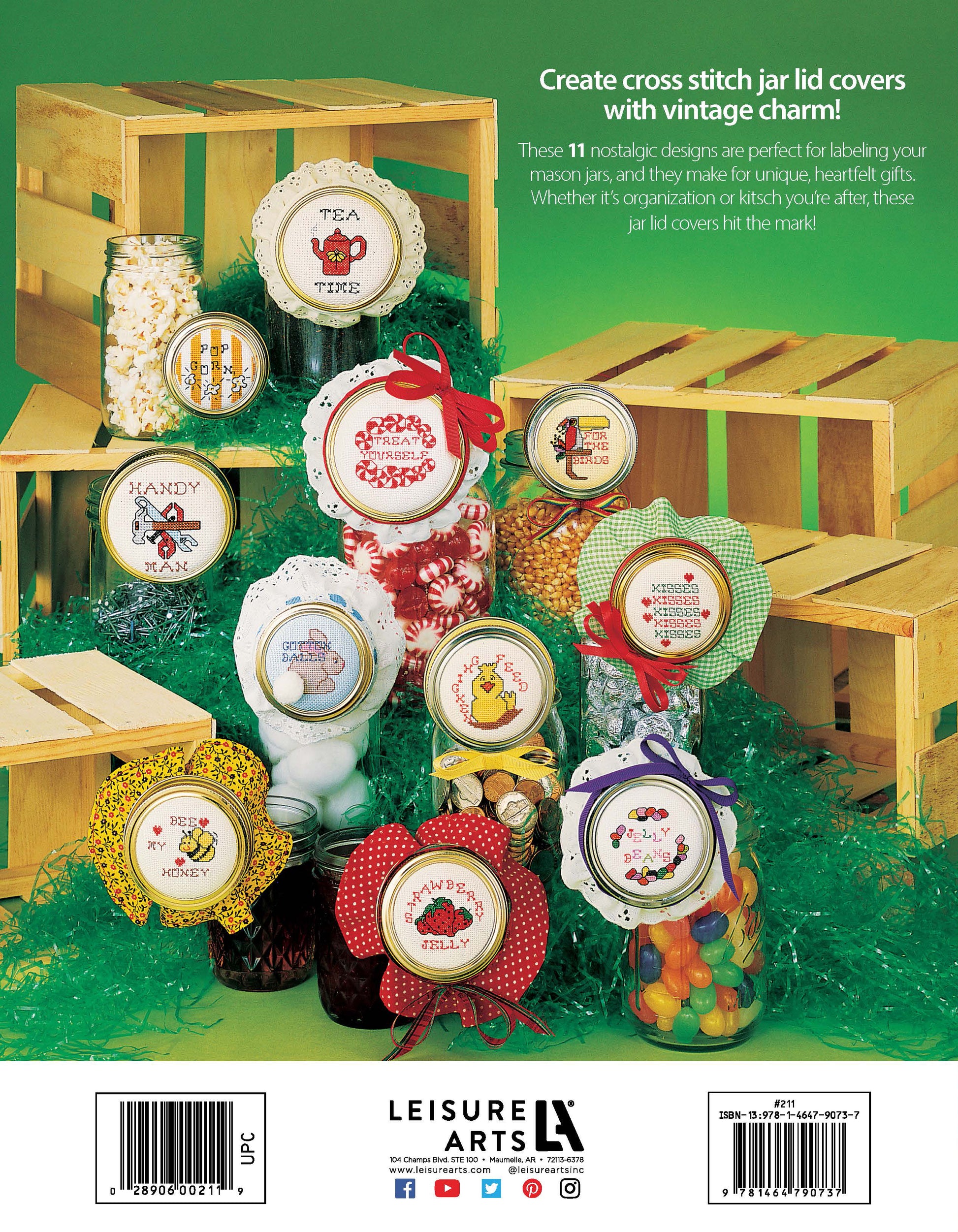 A display features mason jars with colorful candies and vintage cross-stitched lids, using Leisure Arts' "Jar Lids Charted for Cross Stitch" digital download, with cute label designs and beginner labeling tips on green grass and wooden crates.