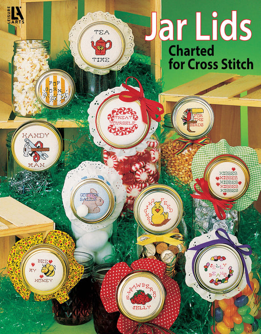 A digital download from Leisure Arts, "Jar Lids Charted for Cross Stitch," features colorful cross-stitched jar lids with cute labels like Tea Time and Bees Honey, finished with ribbons and displayed on green shredded paper.
