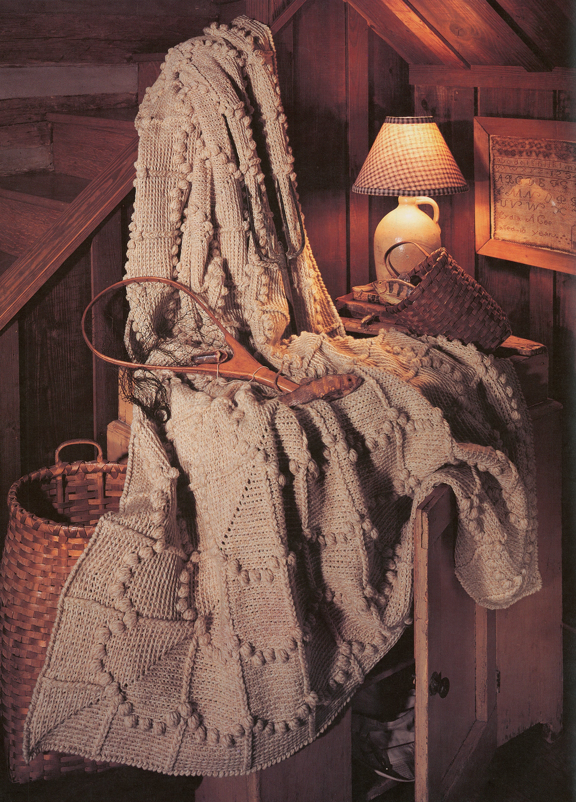 The “Rustic Warmth—11 Afghans” book by Leisure Arts features 9 crochet and 2 knit designs, shown here with a textured cream afghan draped over a wooden chair in a cozy, rustic room.