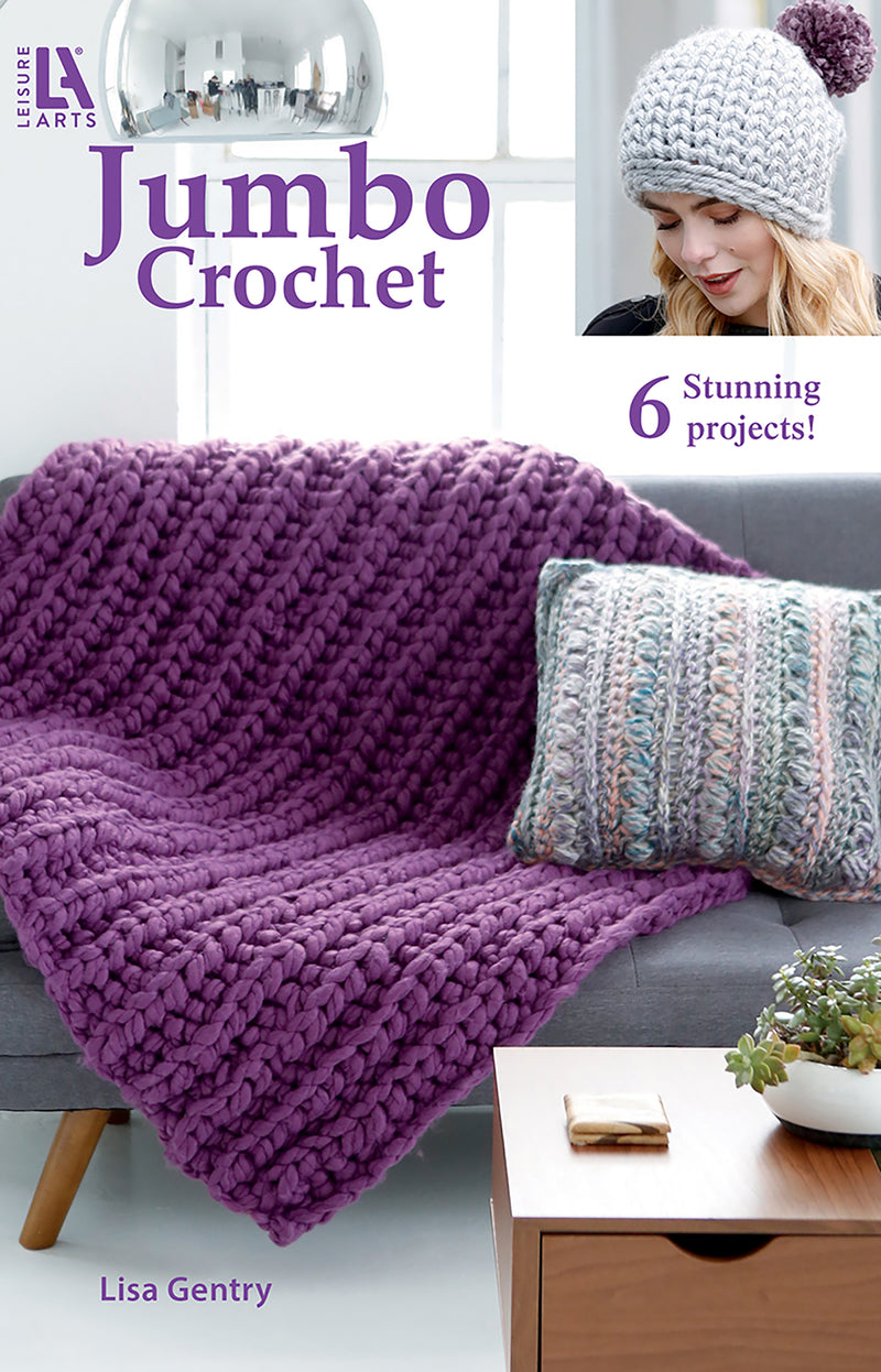 Leisure Arts' Jumbo Crochet features a thick purple blanket on a grey couch, a textured pillow, and an inset of a woman wearing a chunky pom-pom hat, all showcasing projects from the pattern book.