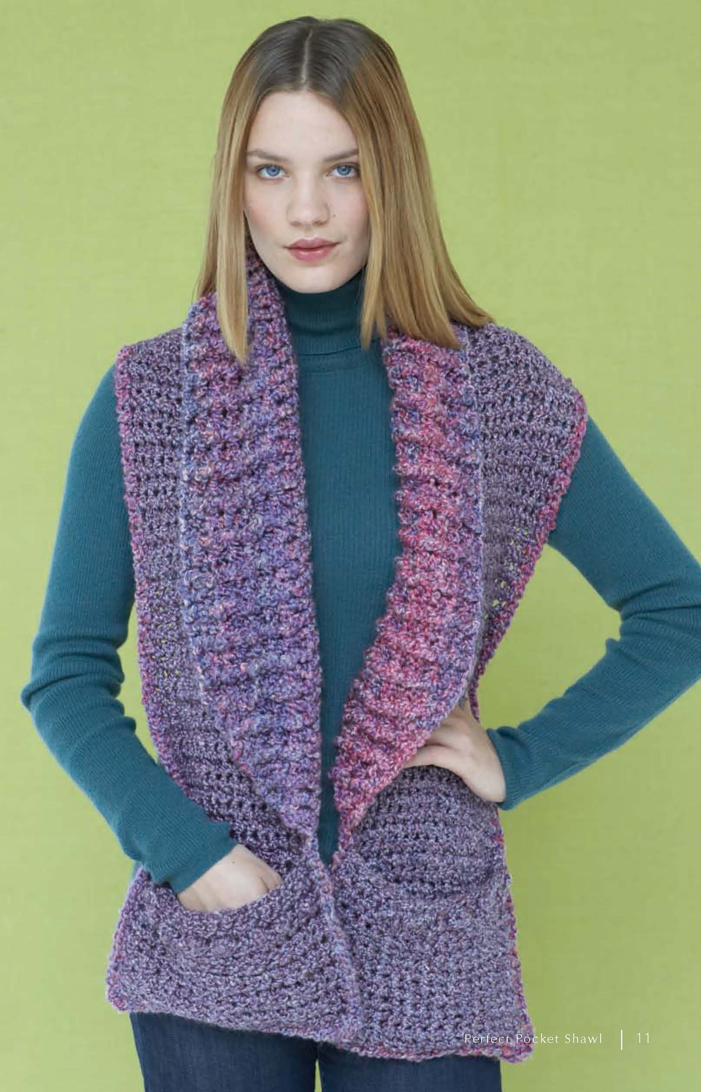 A woman models a chunky purple and pink crochet shawl from "Cozy Cover-Ups—4 Crochet & 2 Knit Designs Created with Lion Brand Homespun" by Leisure Arts, standing against a light green background, hands in her pockets.