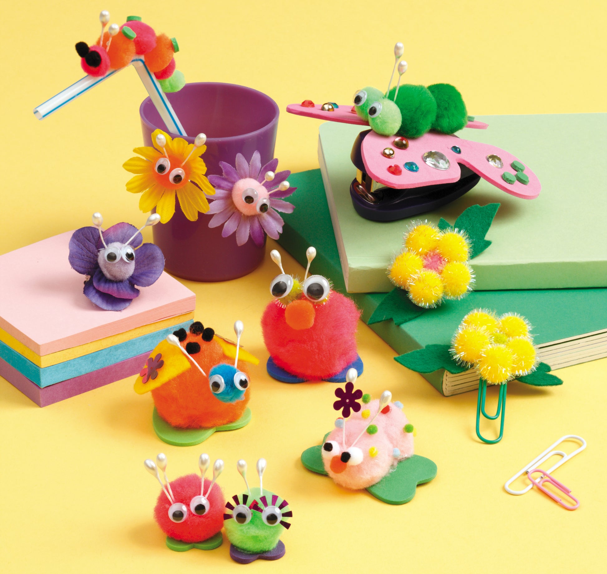 Leisure Arts Pompom Crafts features colorful pom-pom creatures with googly eyes and pipe cleaners, displayed on books, sticky notes, and a purple cup—perfect craft projects for kids.