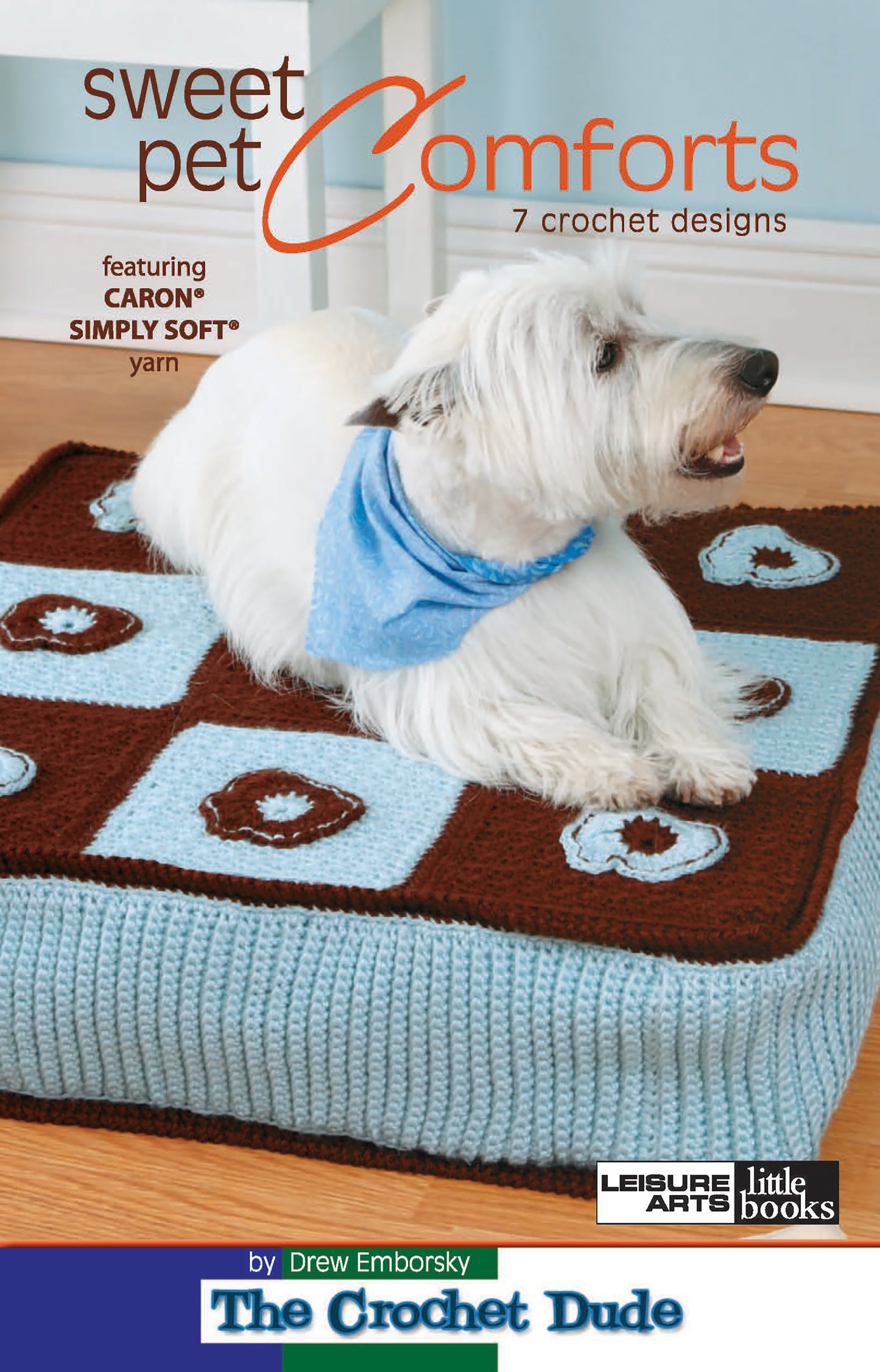 A white dog in a blue bandana sits on a crocheted pet bed with blue and brown squares. The cover displays "Sweet Pet Comforts Digital Download" by Leisure Arts, featuring 7 crochet designs.