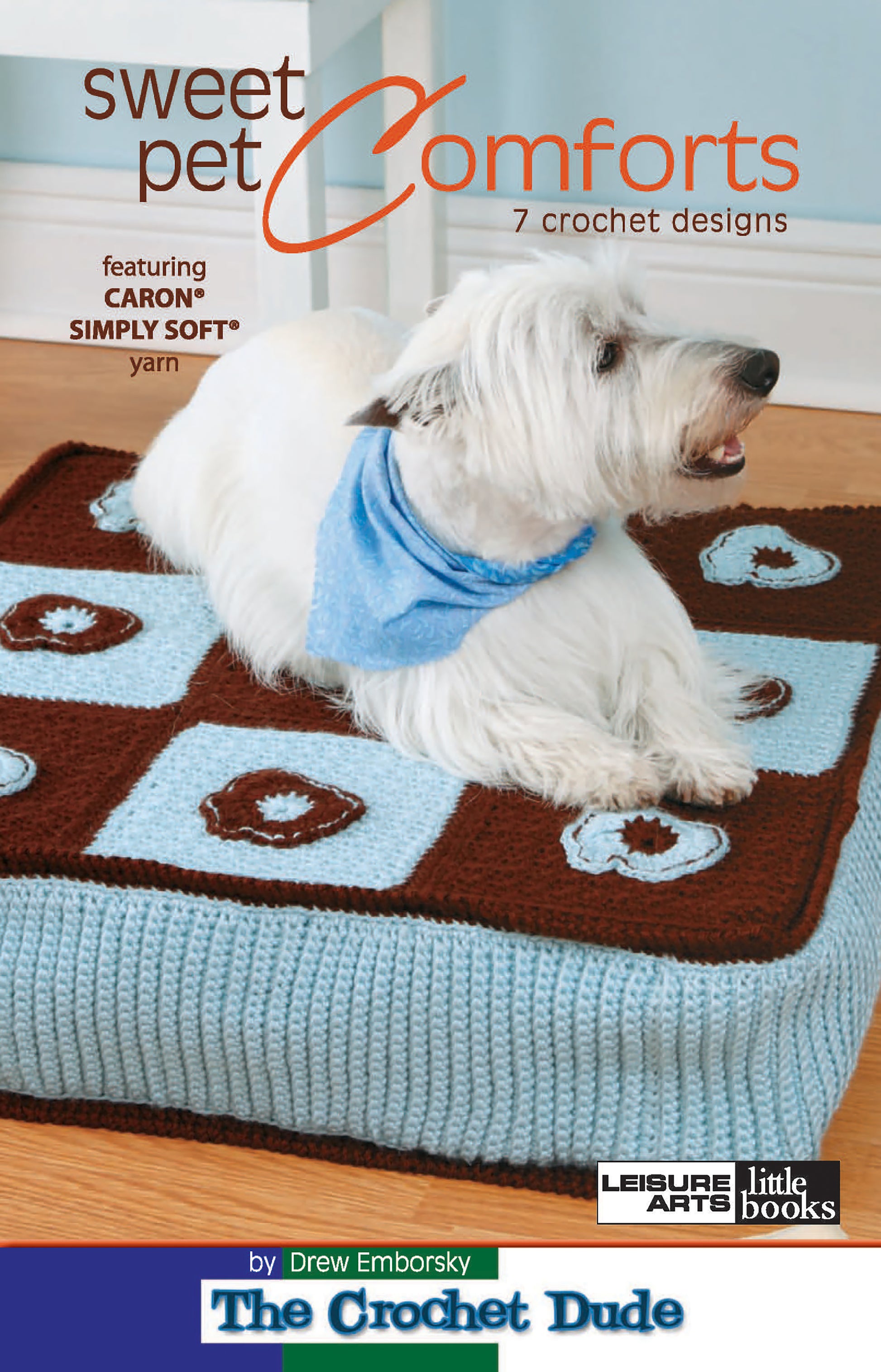 A white dog in a blue bandana sits on a crocheted pet bed with blue and brown squares. The cover displays "Sweet Pet Comforts Digital Download" by Leisure Arts, featuring 7 crochet designs.