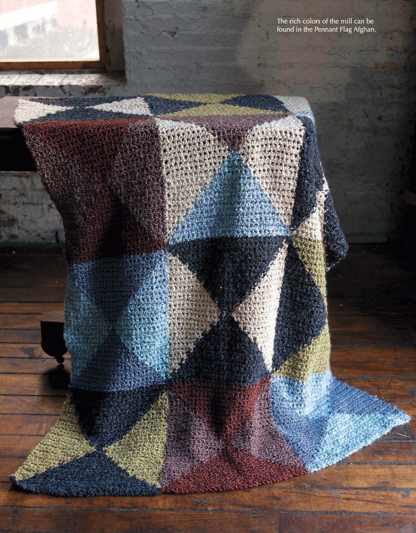 The Story of Homespun Crochet" by Leisure Arts features a bulky yarn afghan with geometric patchwork in blue, green, burgundy, black, and cream—draped on a chair for cozy inspiration.