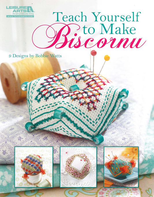 The cover of Teach Yourself to Make Biscornu Digital Download by Leisure Arts displays a cross-stitched biscornu pincushion with colorful pins and three smaller images of biscornu embroidery designs at the bottom.