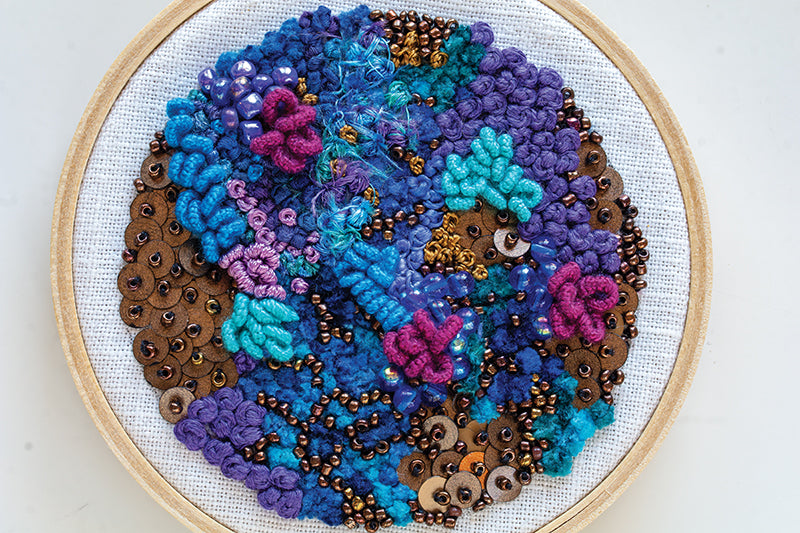 Creative Stitches for Contemporary Embroidery, Volume 2 by C&T Publishing features abstract blue, purple, and turquoise needlework with pink florals, gold sequins, and bronze beads on white fabric, inspired by crazy quilting techniques.