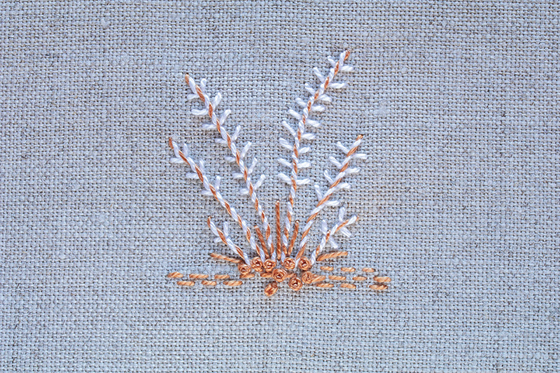 Minimalist grass-like plants with brown stems and white leaves adorn light grey fabric, showcasing elegant hand embroidery from "Creative Stitches for Contemporary Embroidery, Volume 2" by C&T Publishing.