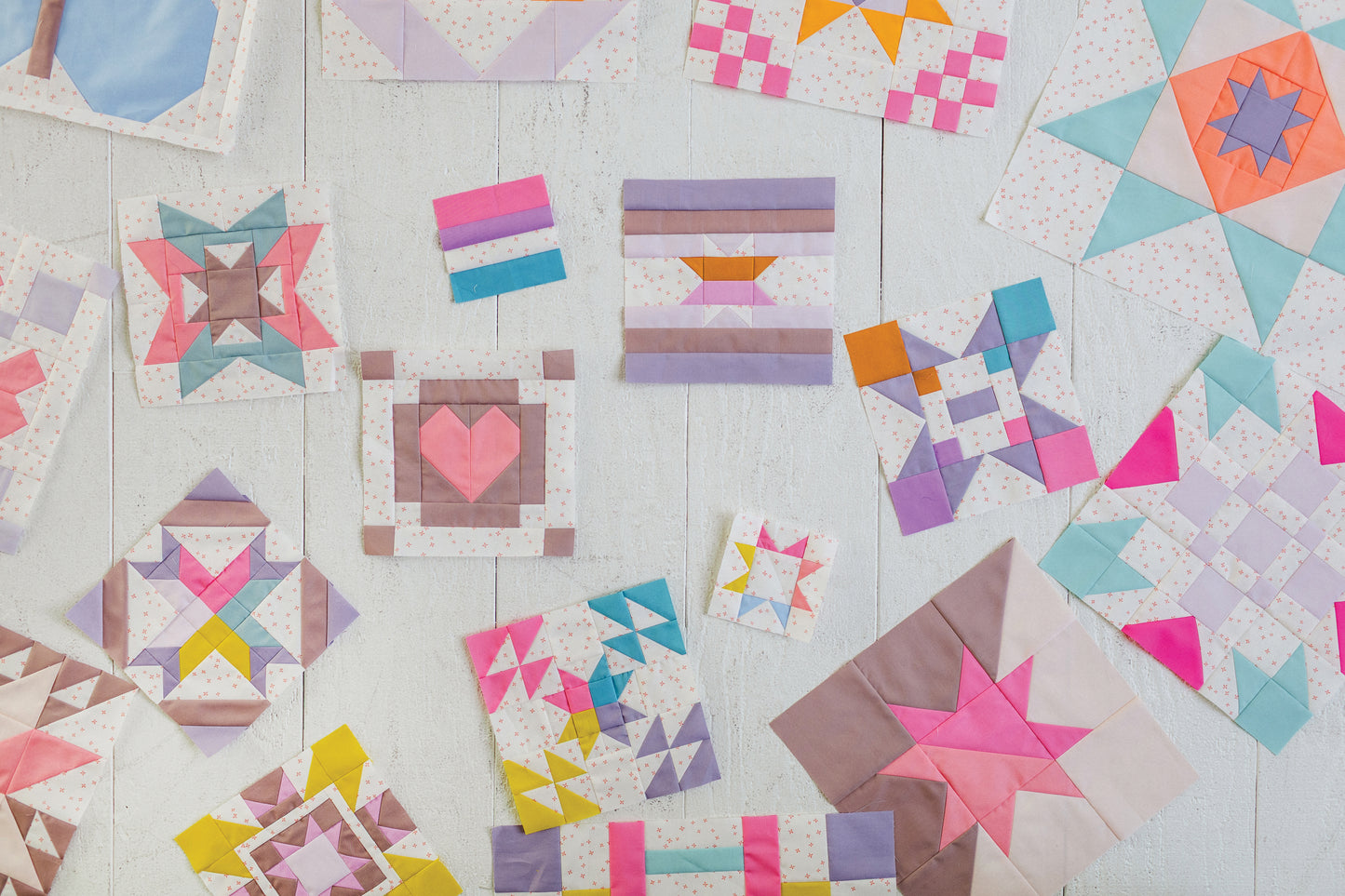 Patchwork Playground by Stash Books features modern quilt blocks with stars, hearts, and squares in pastel and bright fabrics, arranged on a white wooden surface that highlights unique geometric patterns.