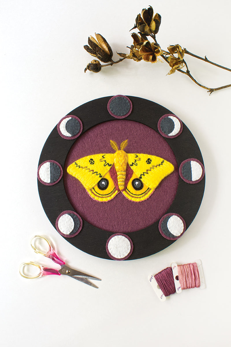The Stash Books "Felt & Thread" features a circular felt appliqué artwork with a yellow moth at the center, black and white circles, plus embroidery scissors, spools of thread, and dried flowers arranged on a white background.