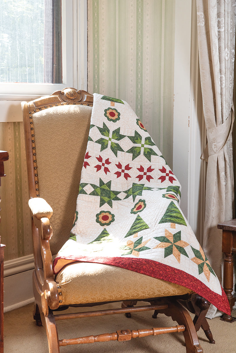 A beige upholstered wooden rocking chair with C&T Publishing's Elm Creek Quilts Christmas draped over the back sits by a window in a sunlit, vintage-style room.