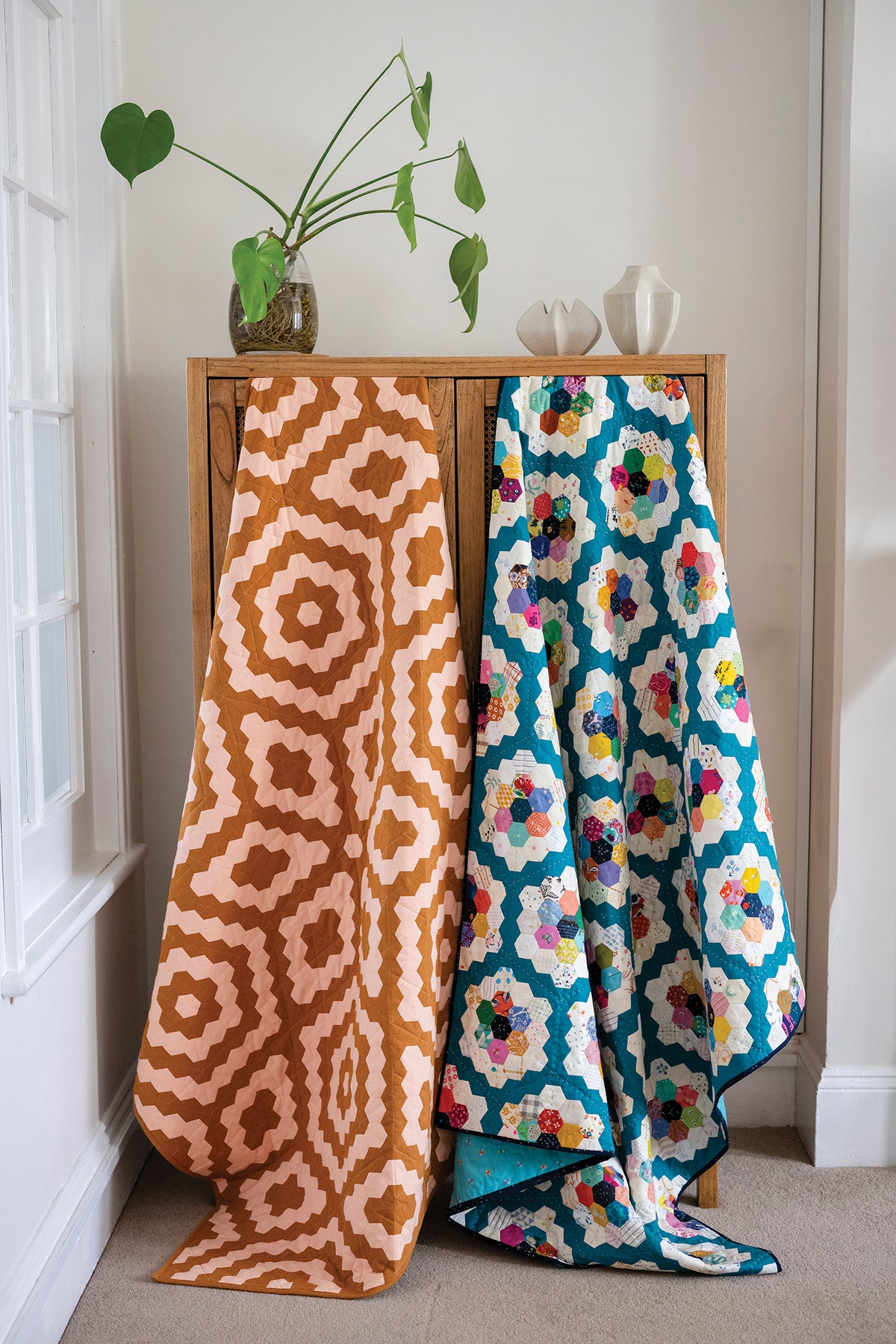 Two 50 Hexagon Quilts created with English paper piecing draped over a wooden cabinet.
