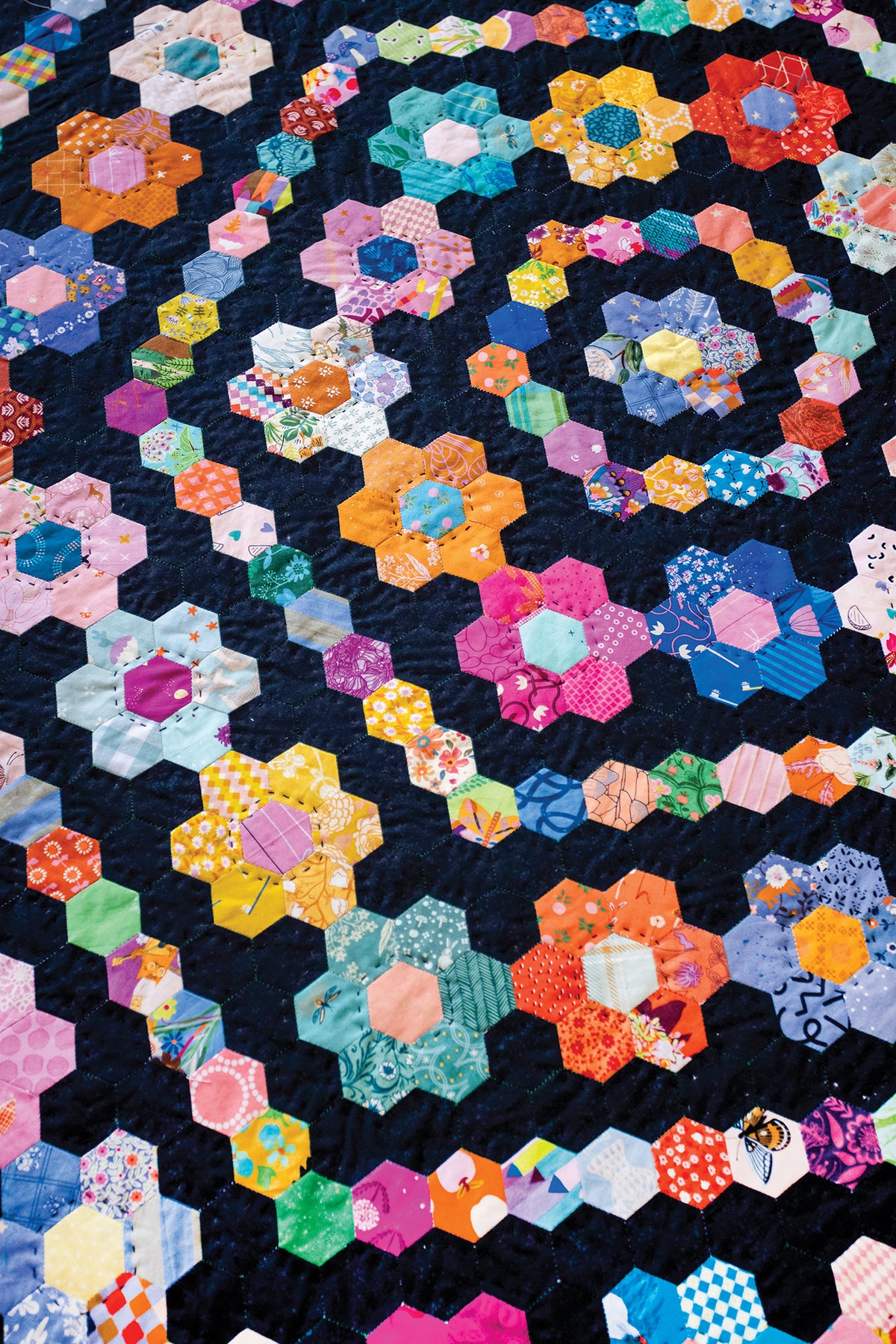 50 Hexagon Quilts top featuring a pattern of colorful English paper piecing hexagons arranged in circular clusters against a dark navy background.