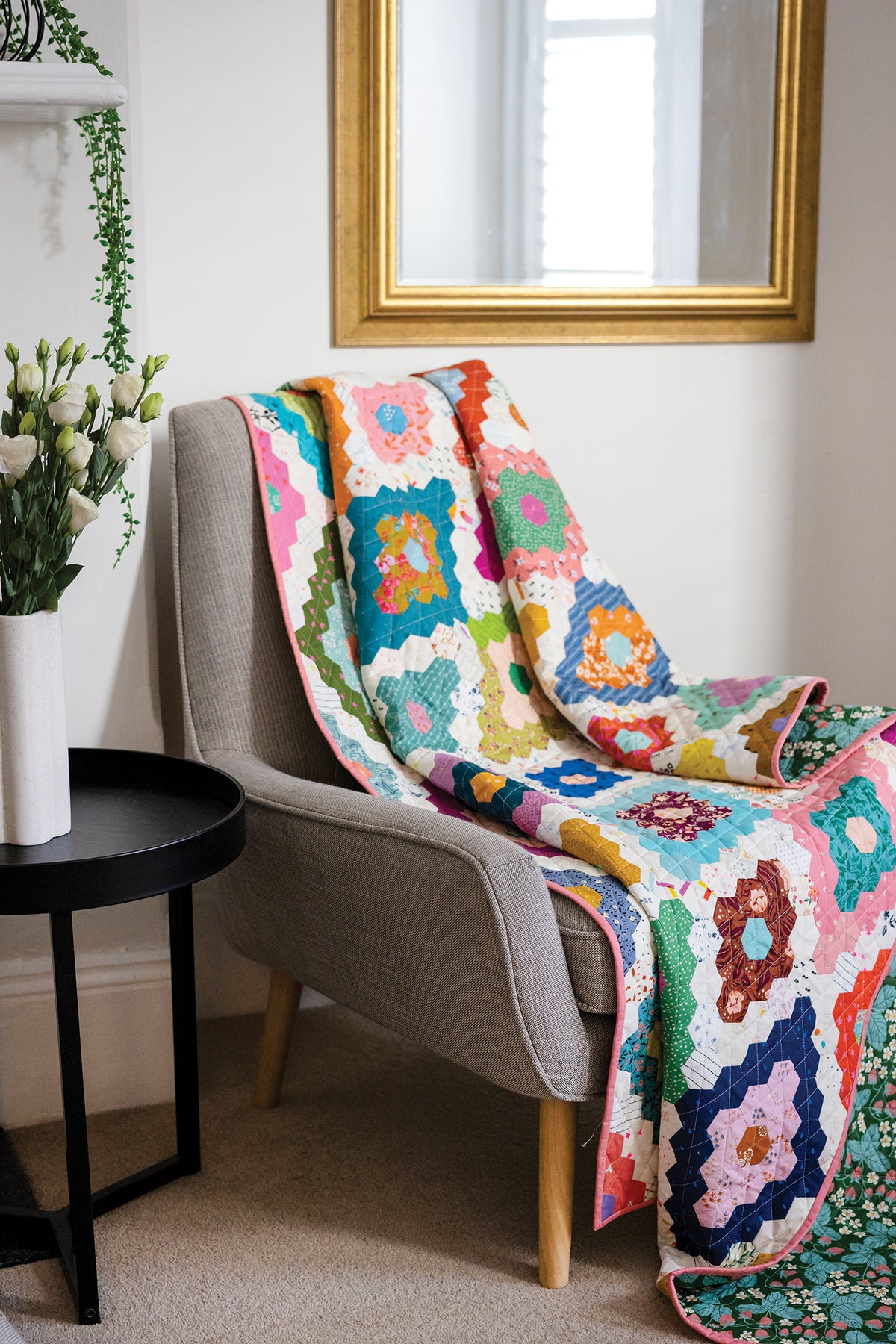 A colorful 50 Hexagon Quilts project featuring a repeating pattern of hexagons draped over a grey armchair.