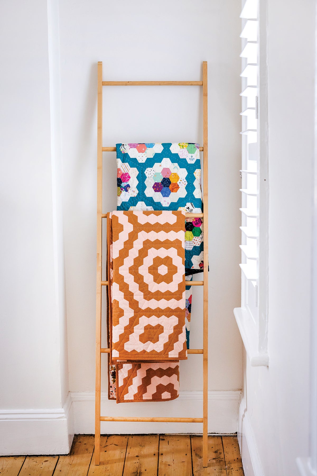 Two 50 Hexagon Quilts handmade with hexagon patterns draped over a wooden ladder leaning against a white wall.