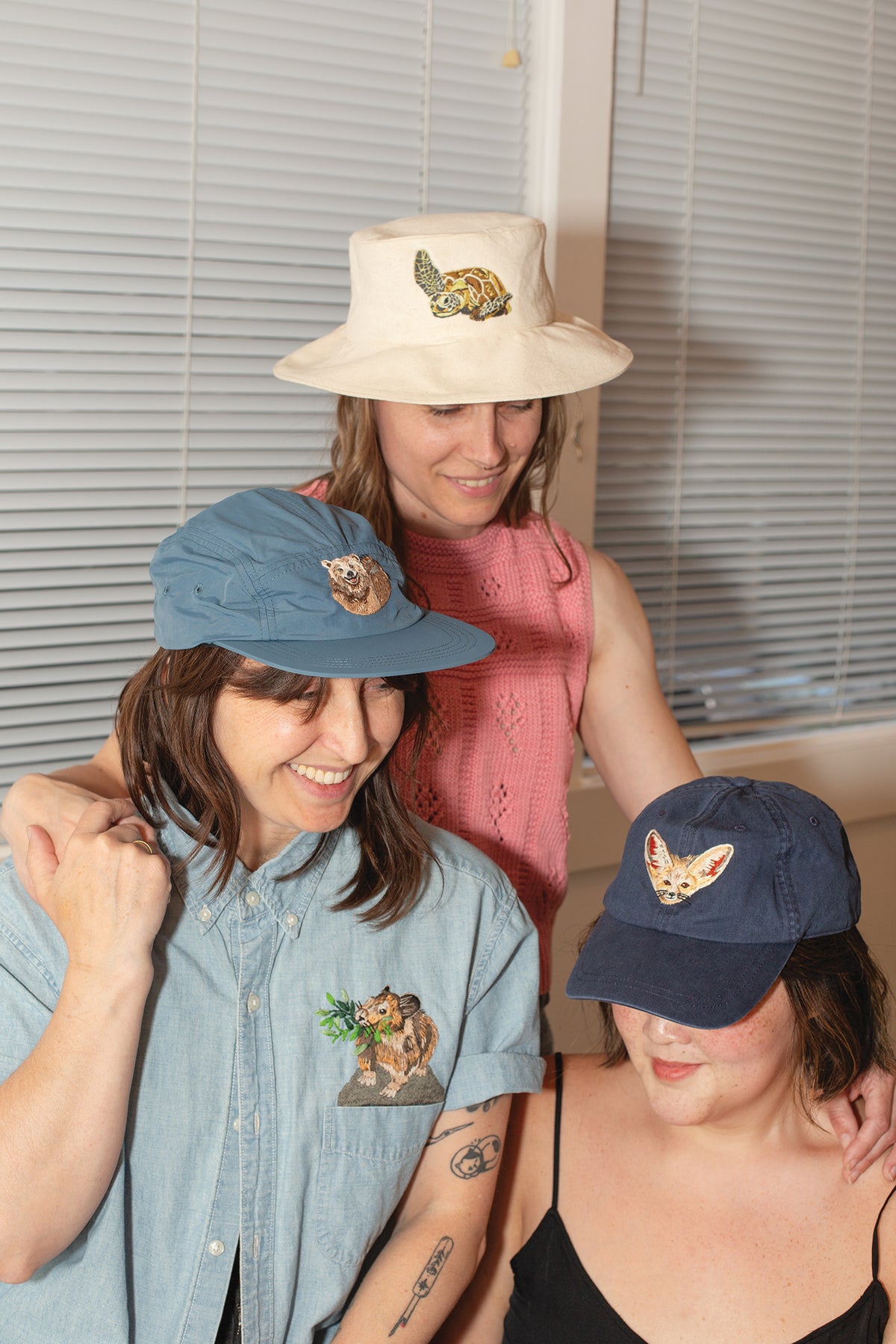 Three people wear Wild & Wearable Animal Embroidery shirts featuring handmade detailed embroidery of a turtle, a quokka, and a fennec fox.